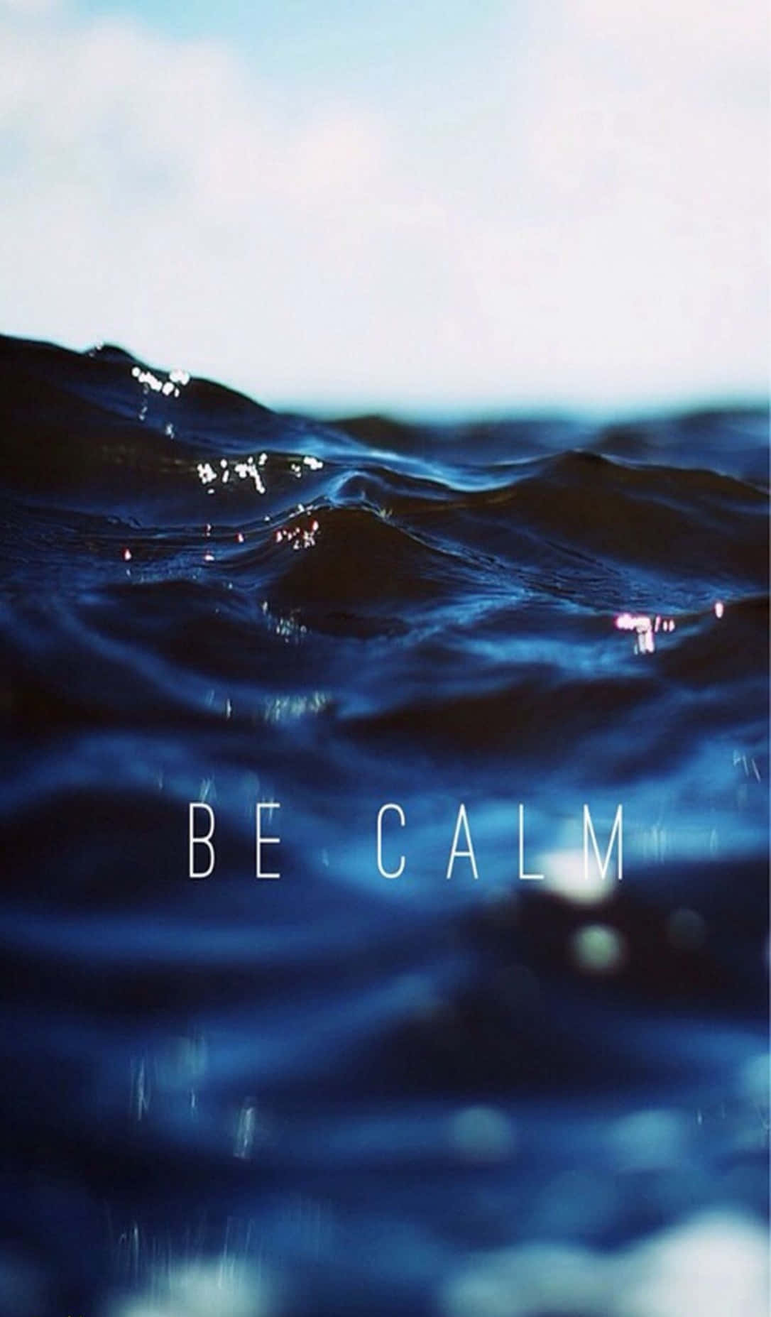 Calm Aesthetic 桌布 壁紙 — 平靜的海浪在柔和藍天下泛起漣漪，水面上漂浮著「BE CALM」文字。