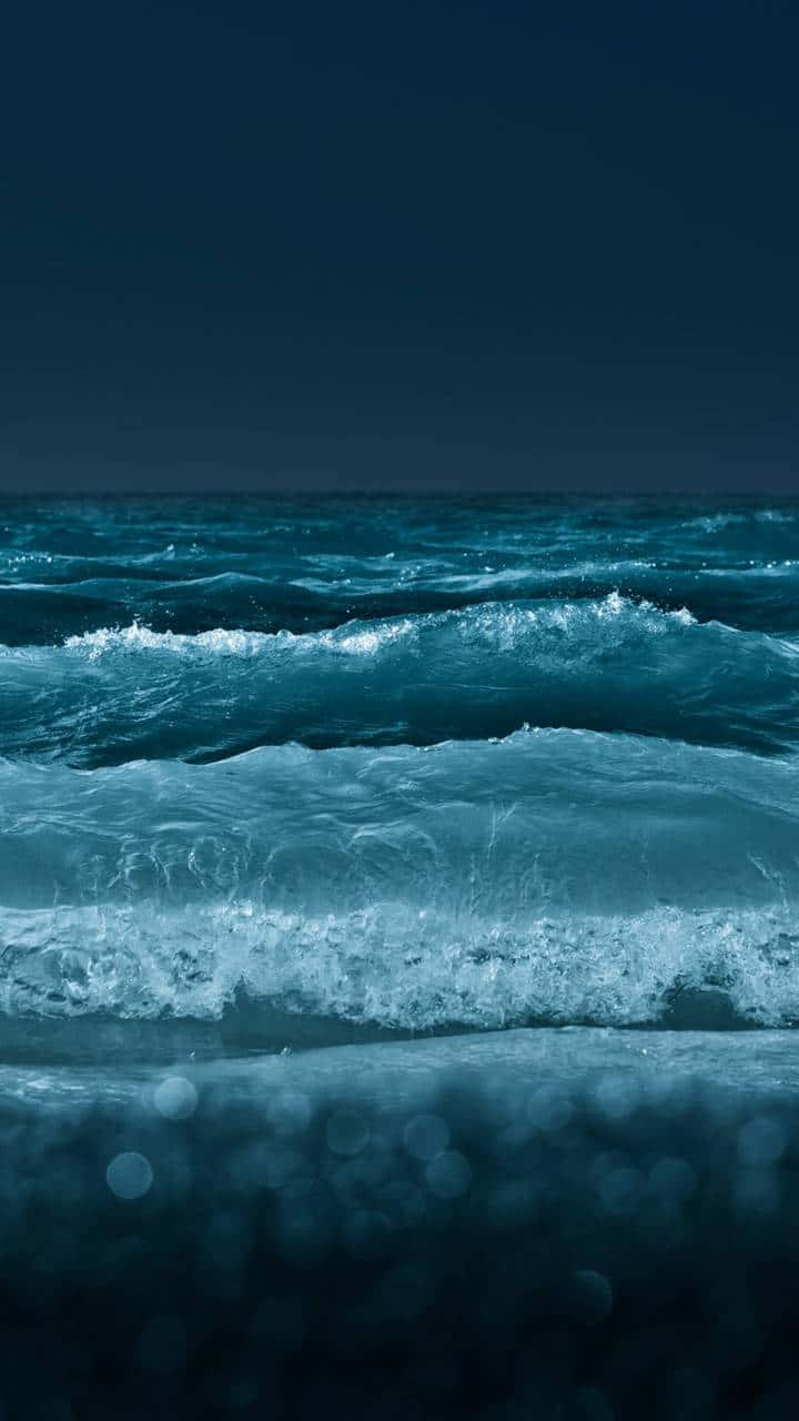 水 桌布 壁紙 — 平靜的海浪在漆黑的夜空下向岸邊翻滾，前景有散景燈光。