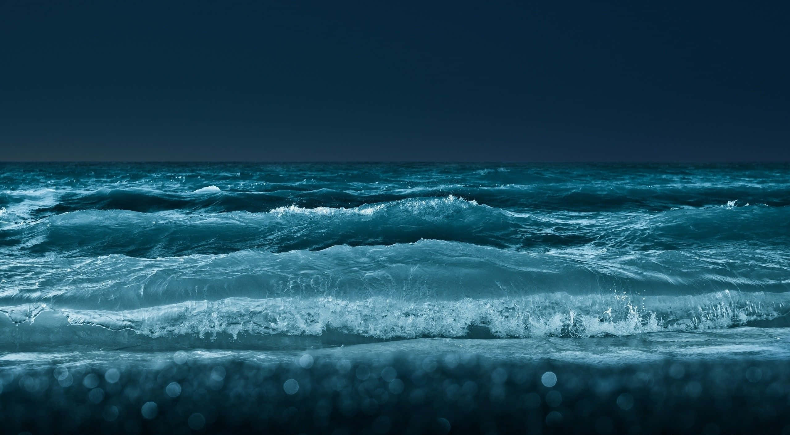 桌布 壁紙 — 平靜的海浪在漆黑的夜空下翻滾，散景燈光映照在濕沙上。