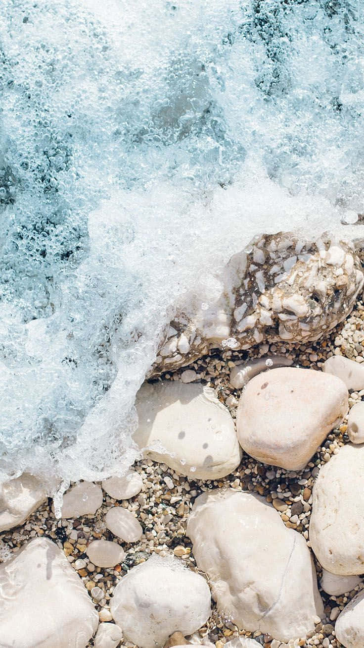 預科生美學 桌布 壁紙 — 平靜的海浪沖刷著陽光明媚的海灘上光滑的白色和灰色鵝卵石。