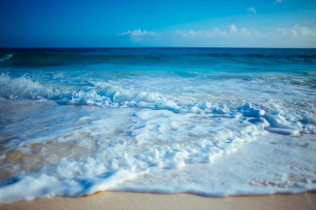 Beach Waves 桌布 壁紙 — 平靜的碧綠海浪輕輕拍打陽光照耀的沙灘，天空湛藍清澈，白雲點點。