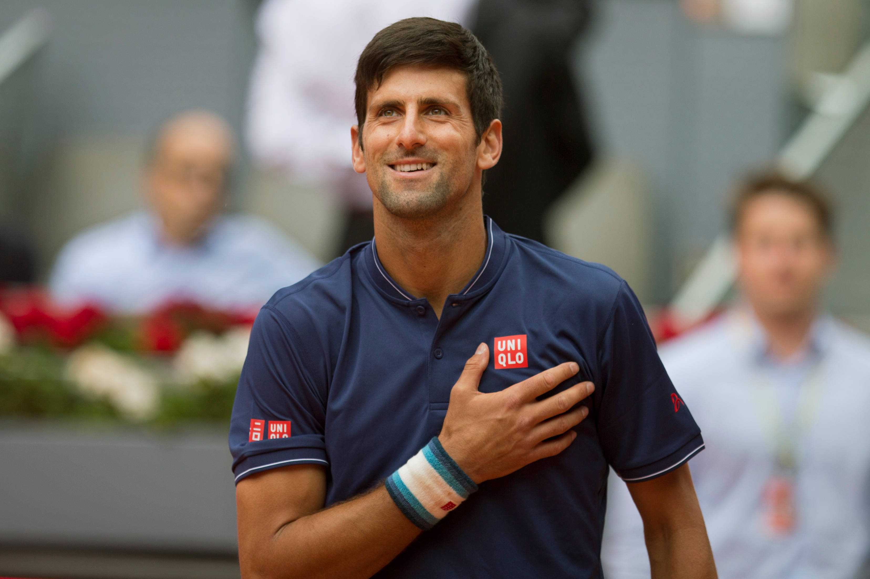 Novak 桌布 壁紙 — 平靜的網球選手諾瓦克·喬科維奇在比賽中穿著海軍藍Uniqlo Polo衫，手放在心口微笑。