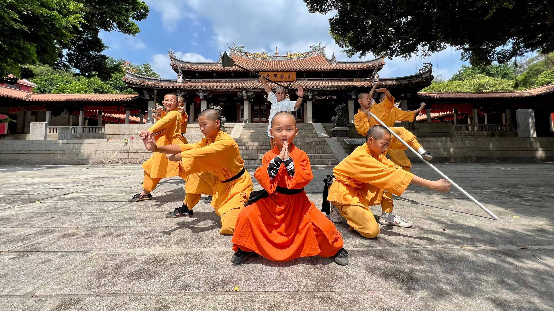 Exercise 桌布 壁紙 — 年輕僧侶身穿鮮豔橙色僧袍，在晴朗藍天下於寺廟庭院練習武術姿勢。