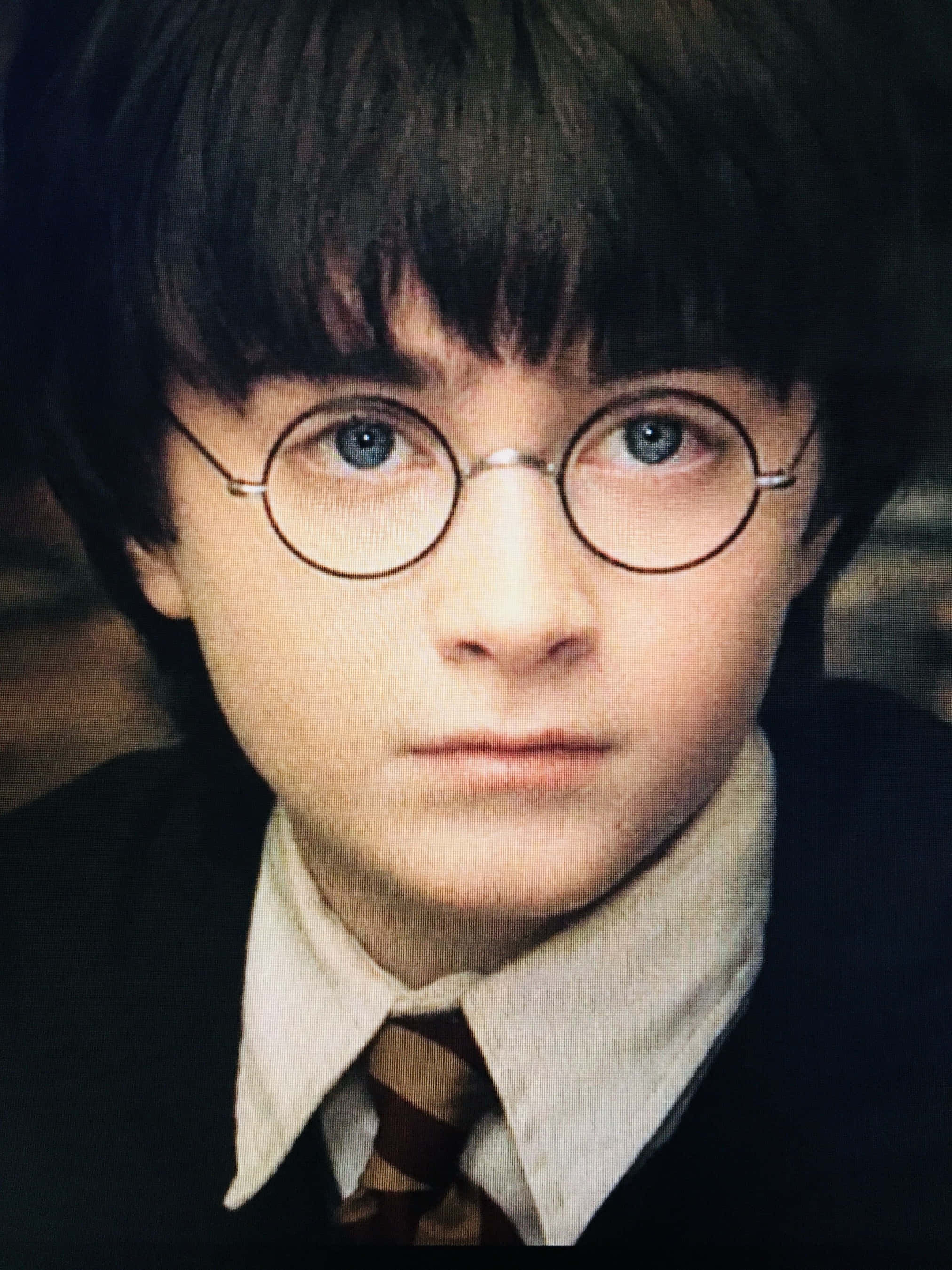 Harry Potter Profile 桌布 壁紙 — 年輕哈利波特戴圓眼鏡、表情嚴肅、身穿校服的近距離肖像。