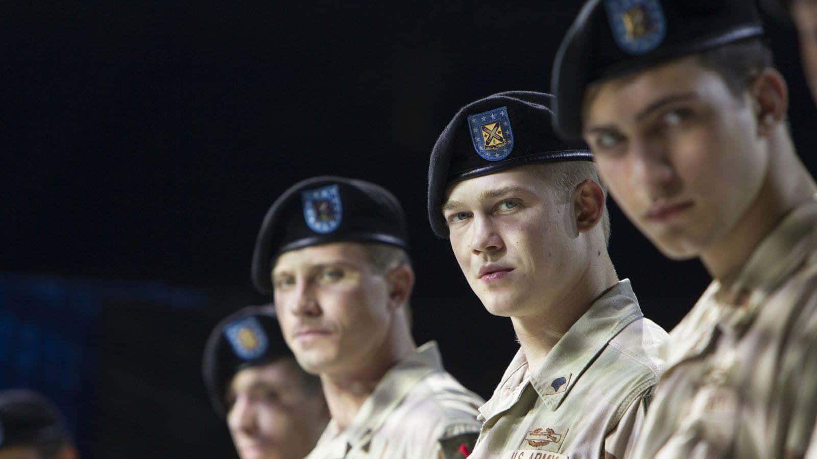 Joe Alwyn 桌布 壁紙 — 年輕士兵身穿制服，在昏暗燈光下以嚴肅的表情列隊站立。