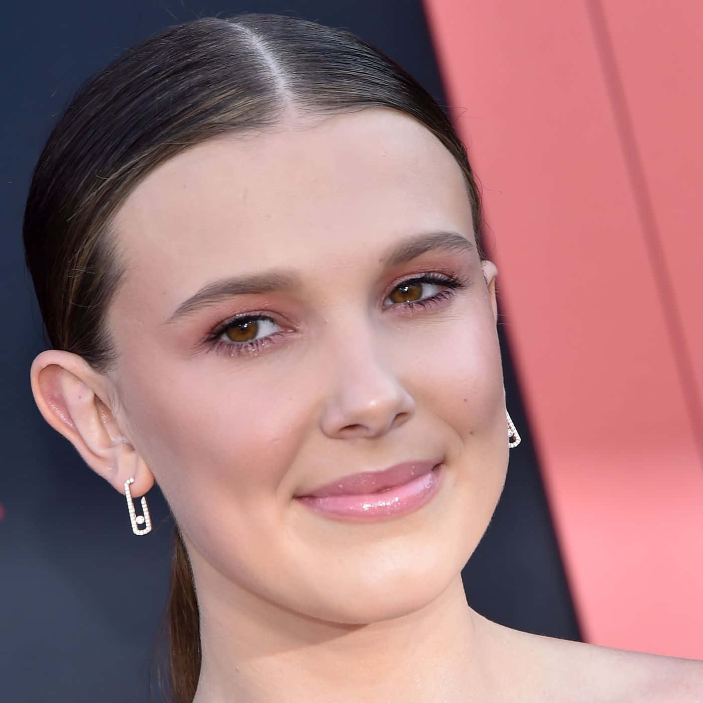 Celebrity 桌布 壁紙 — 年輕女子特寫肖像，深色頭髮向後梳，在粉紅和黑色幾何背景前輕柔微笑。