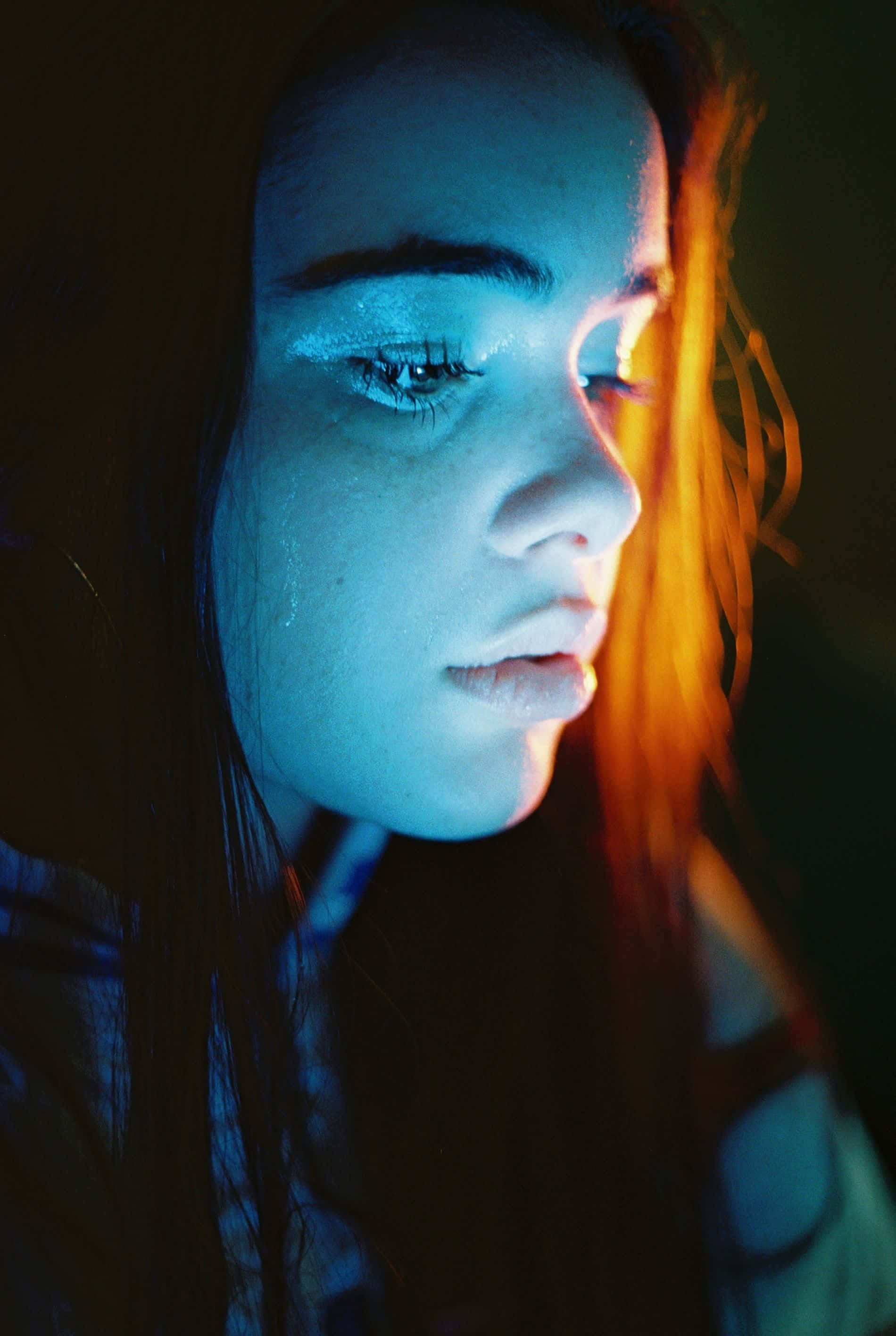 emotion 桌布 壁紙 — 年輕女子的臉龐在深色背景下沐浴在對比鮮明的藍色和橙色霓虹燈光中。