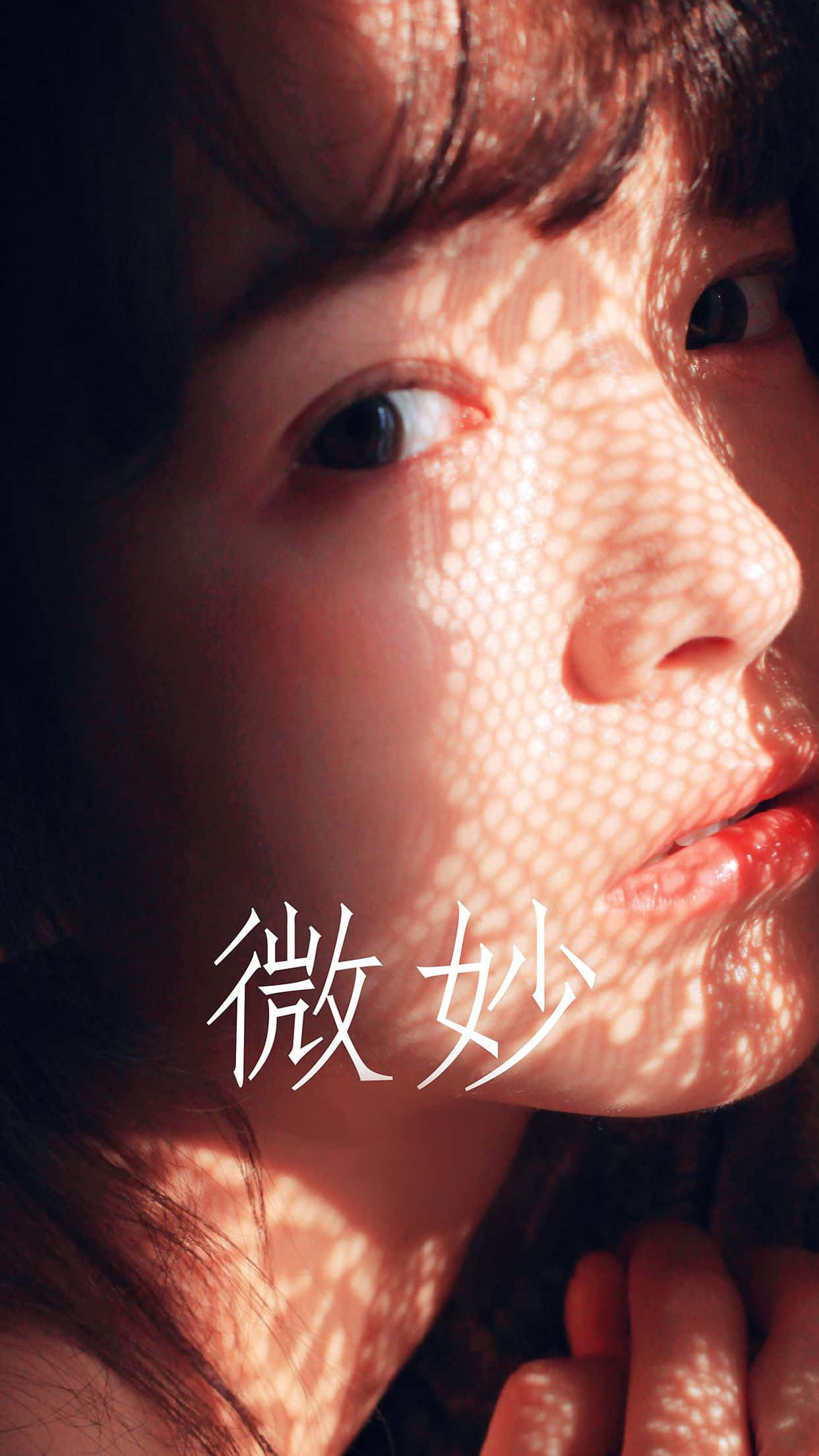 K-pop 桌布 壁紙 — 年輕女子臉部的特寫肖像，沐浴在穿過樹葉的溫暖陽光中，在肌膚上投下斑駁的陰影。