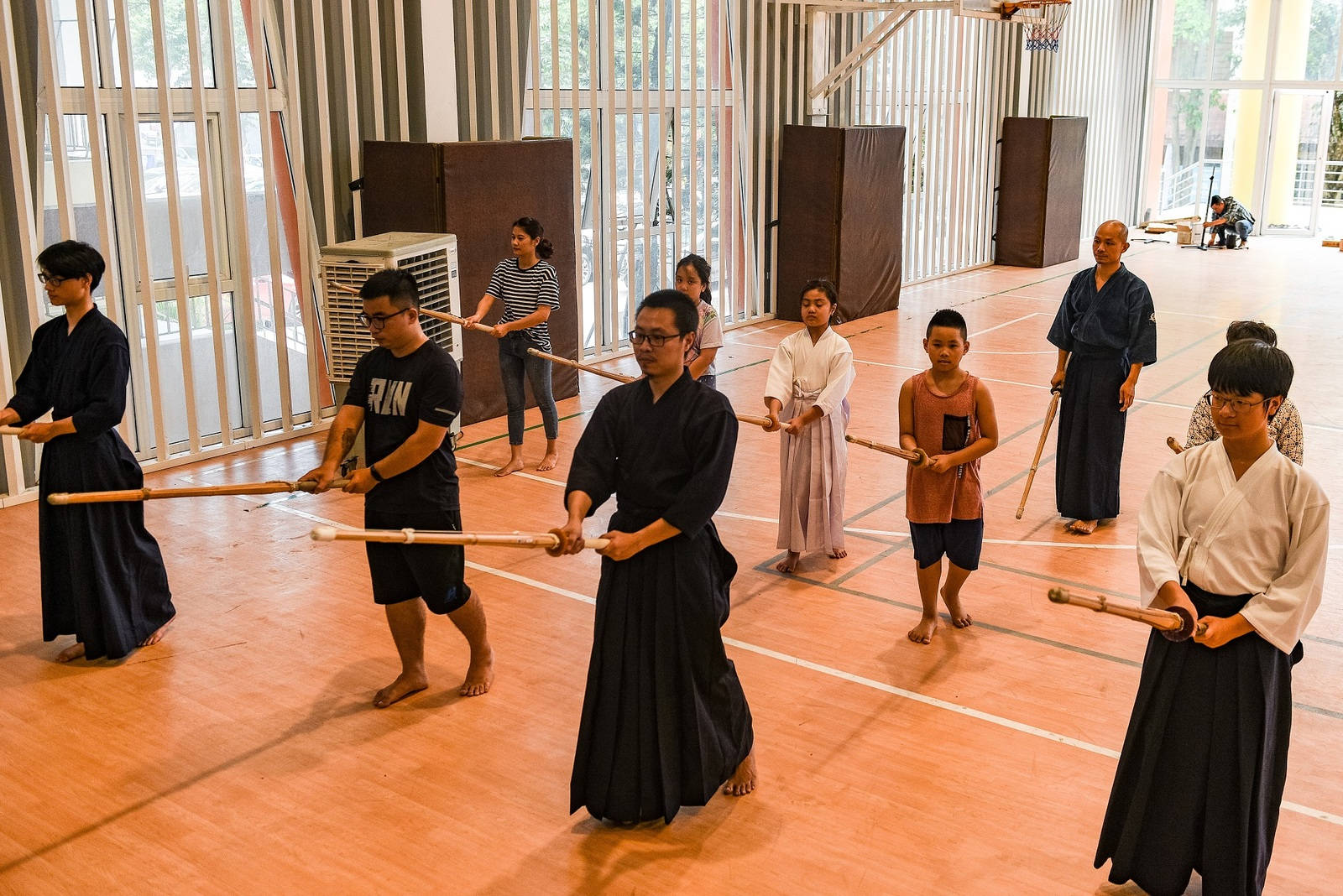 運動 桌布 壁紙 — 年輕武術家穿著傳統服裝，在明亮且有大窗戶的體育館內用木製 bokken 練習。