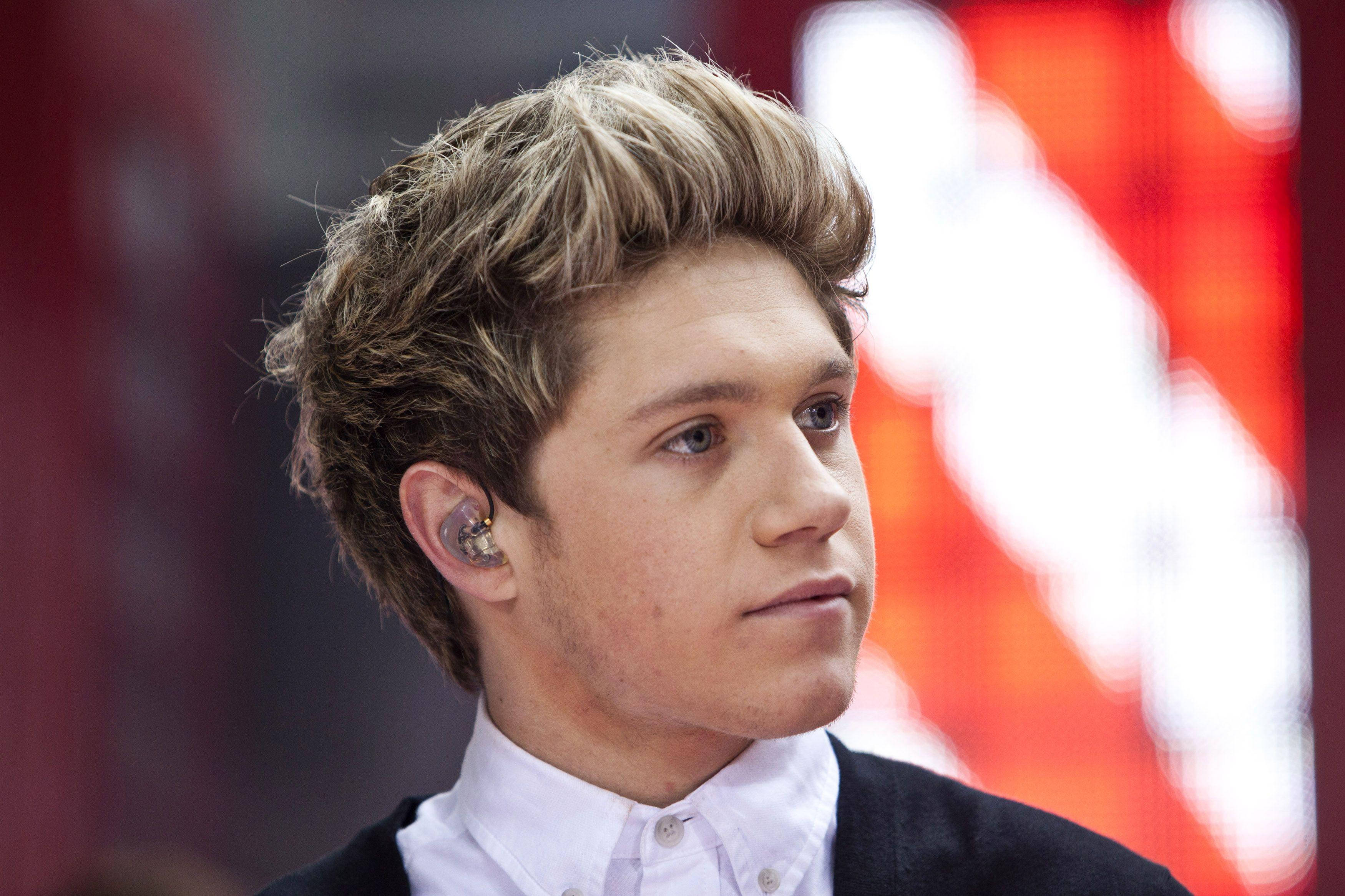 niall horan 桌布 壁紙 — 年輕男子特寫，頭髮造型，佩戴入耳式監聽器，若有所思地側望，背景為模糊的紅色。