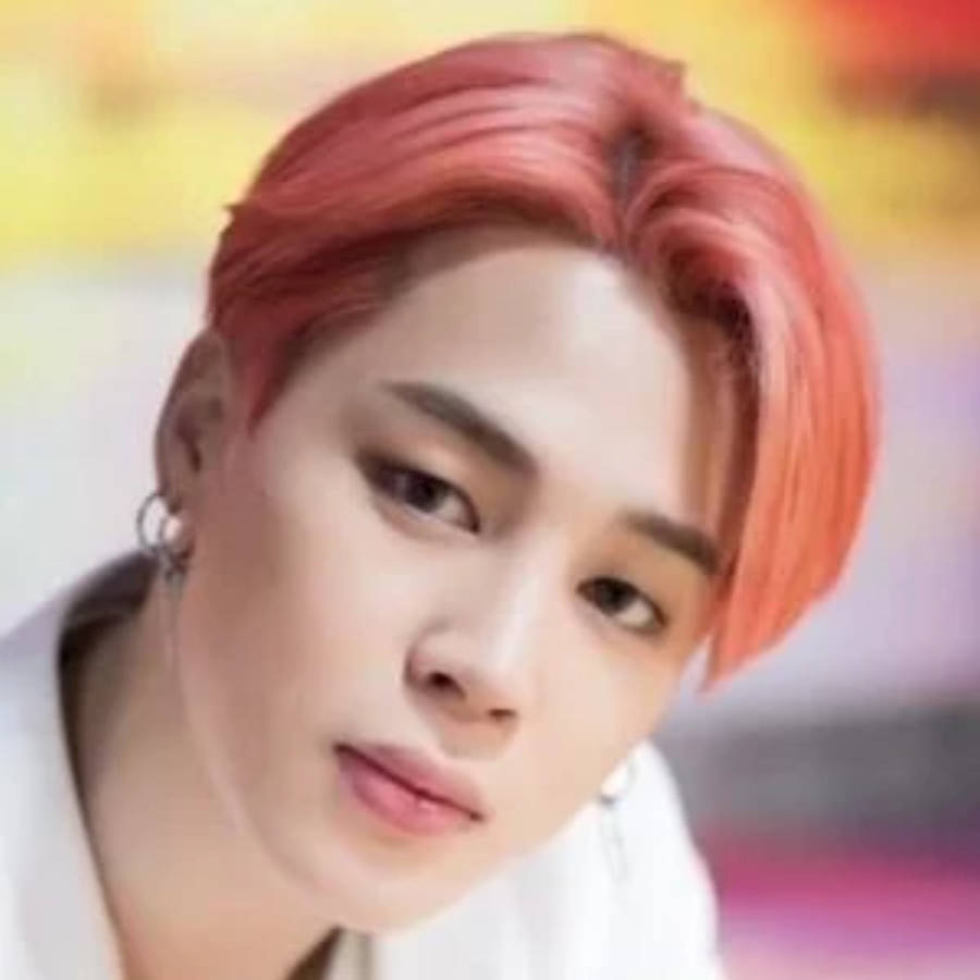 BTS 智旻 桌布 壁紙 — 年輕男子特寫肖像，一頭充滿活力的珊瑚紅髮，柔和眼神，背景模糊多彩。