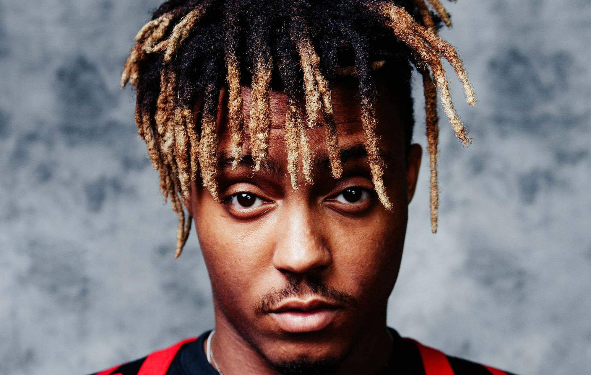 Juice Wrld Desktop 桌布 壁紙 — 年輕男子特寫肖像，帶有紋理辮子和強烈眼神，背景為灰色混凝土牆。