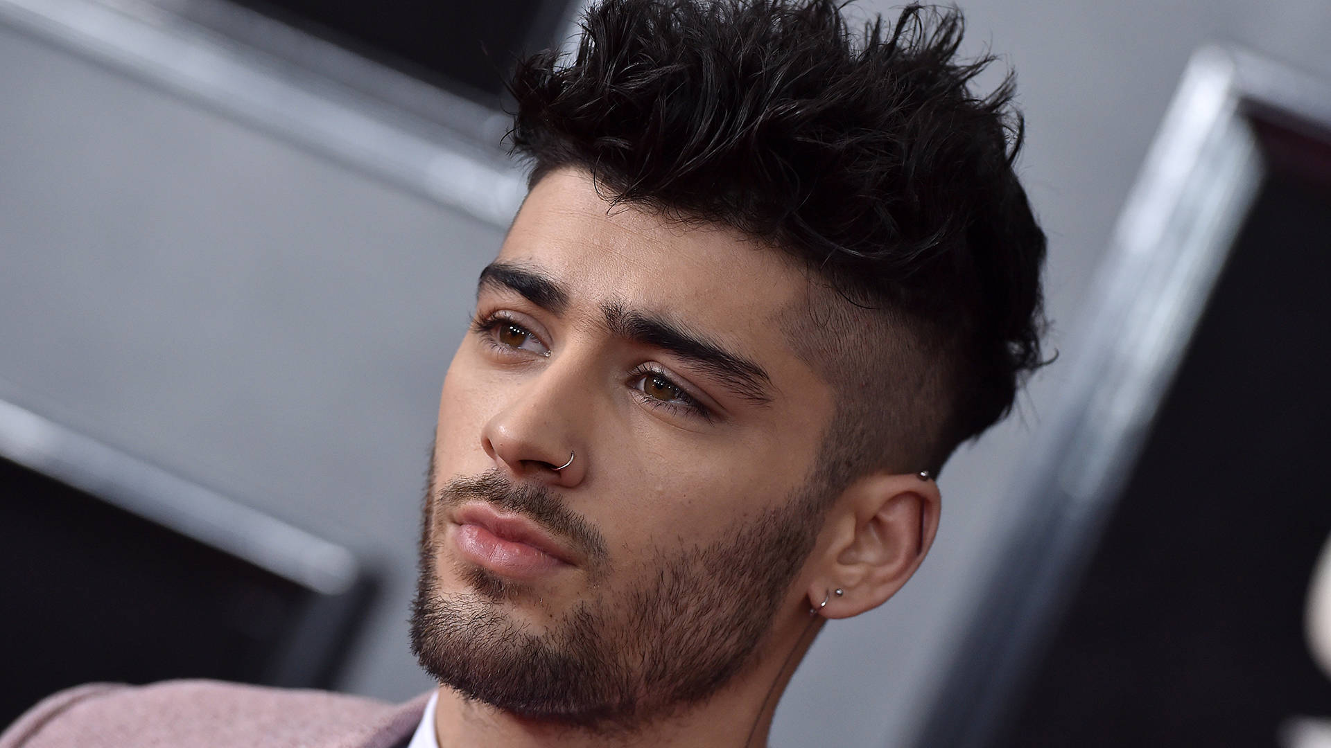 zayn 桌布 壁紙 — 年輕男子特寫肖像，深色刺蝟頭，臉部穿孔，若有所思地望向遠方。