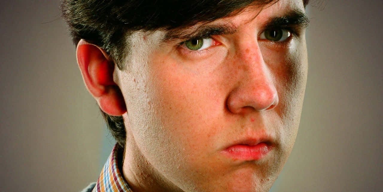 Neville Longbottom 桌布 壁紙 — 年輕男子的特寫肖像，他有強烈的綠色眼睛和深色頭髮，直視鏡頭。