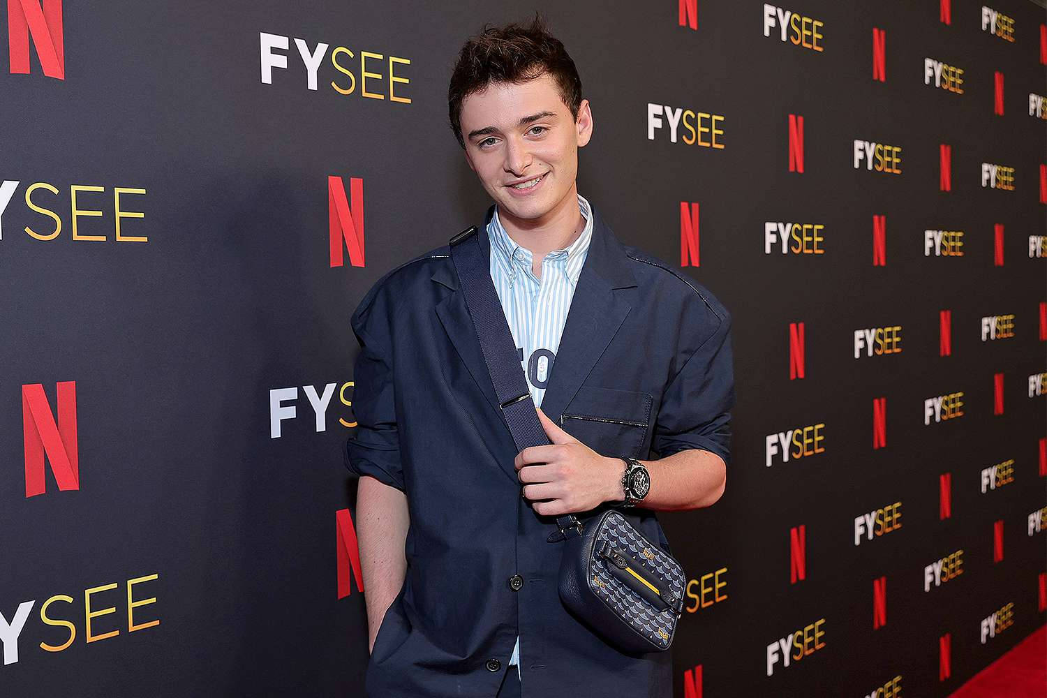 Netflix 桌布 壁紙 — 年輕男子身穿海軍藍西裝外套，手持圖案斜背包，對著重複的Netflix FYSEE背景微笑。