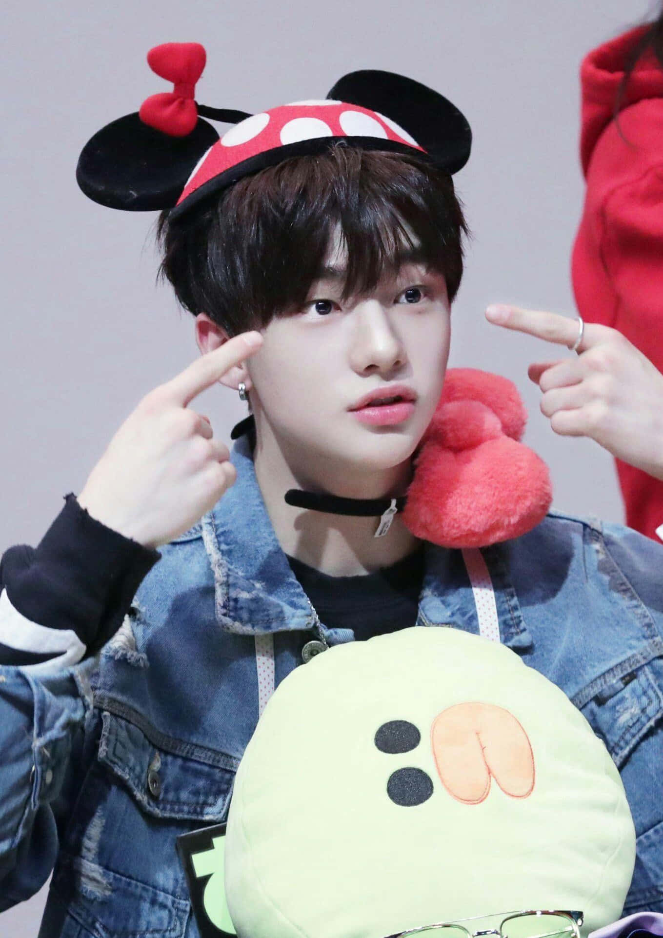 hyunjin 桌布 壁紙 — 年輕男子身穿牛仔外套、戴著米妮老鼠耳朵，一邊指著太陽穴，一邊抱著毛絨玩具。