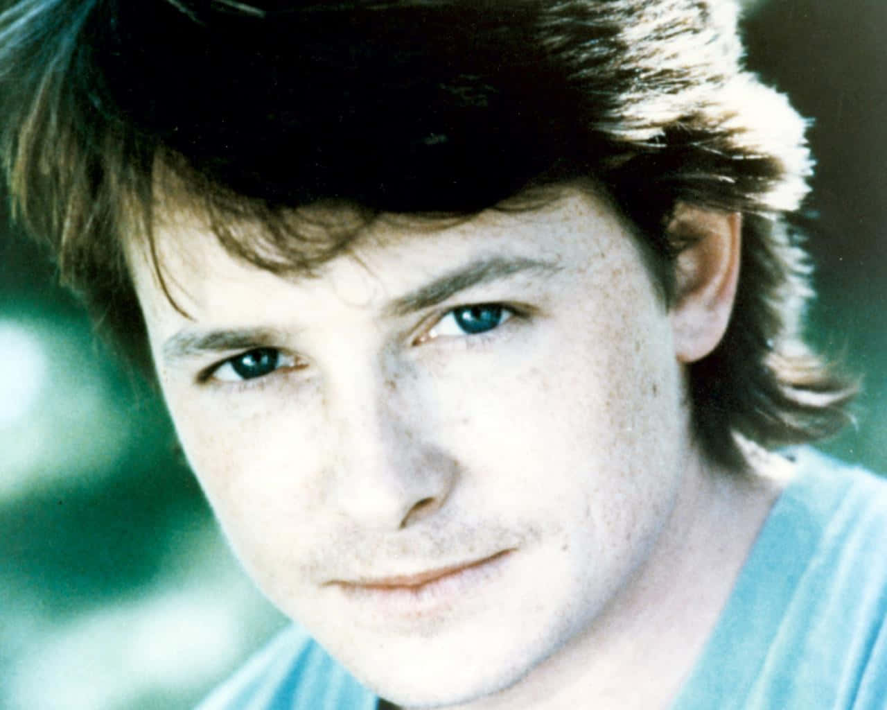 michael j fox 桌布 壁紙 — 年輕男子近距離肖像，臉上有雀斑和藍色眼睛，直視觀眾，背景為柔和綠色。