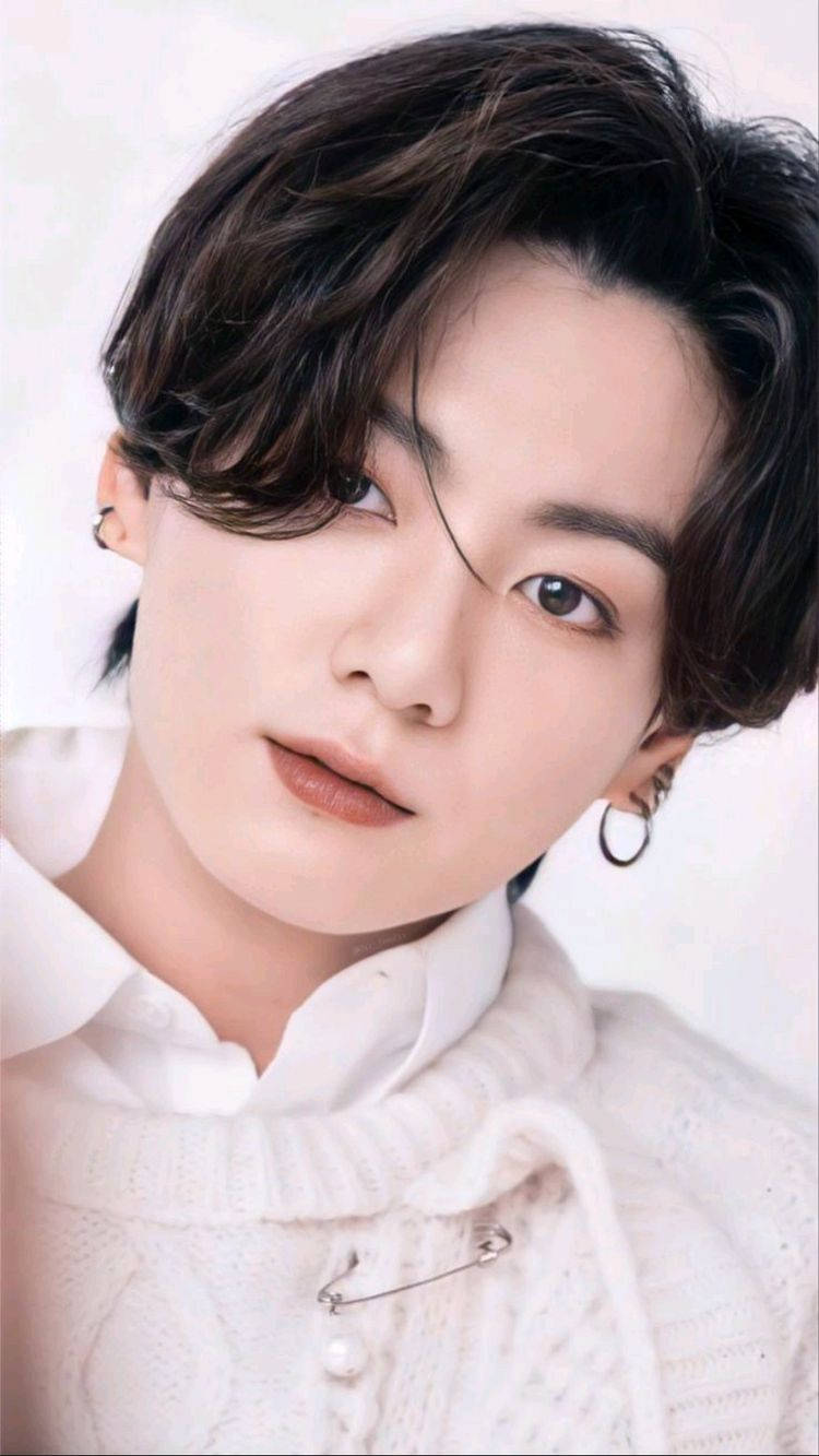 Jungkook 桌布 壁紙 — 年輕男子近距離肖像照，深色波浪頭髮，穿著白色針織毛衣和圓環耳環，背景為柔和白色。