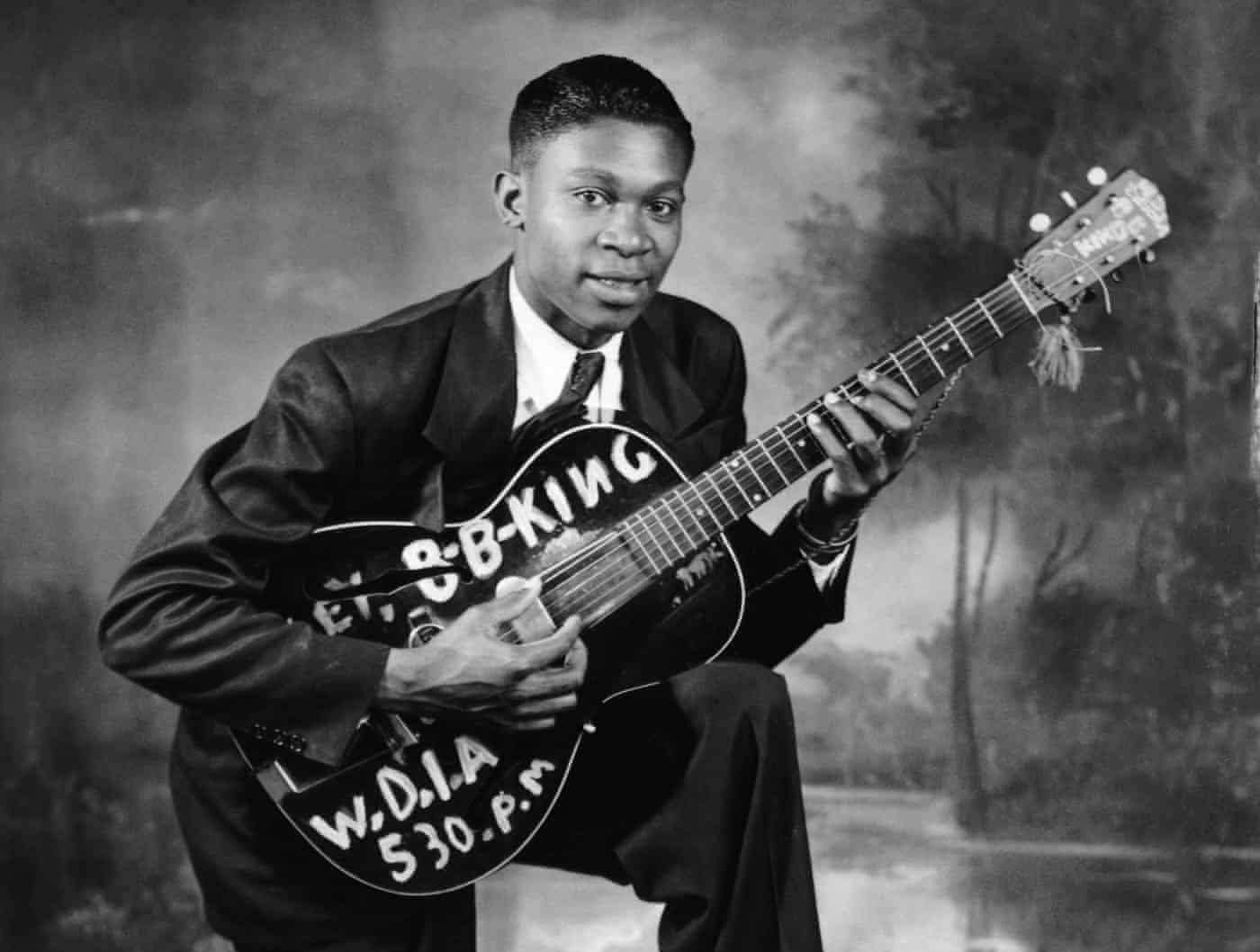 Celebrity 桌布 壁紙 — 年輕的B.B. King身穿西裝，在樹木環繞的攝影棚背景下手持他的標誌性吉他。