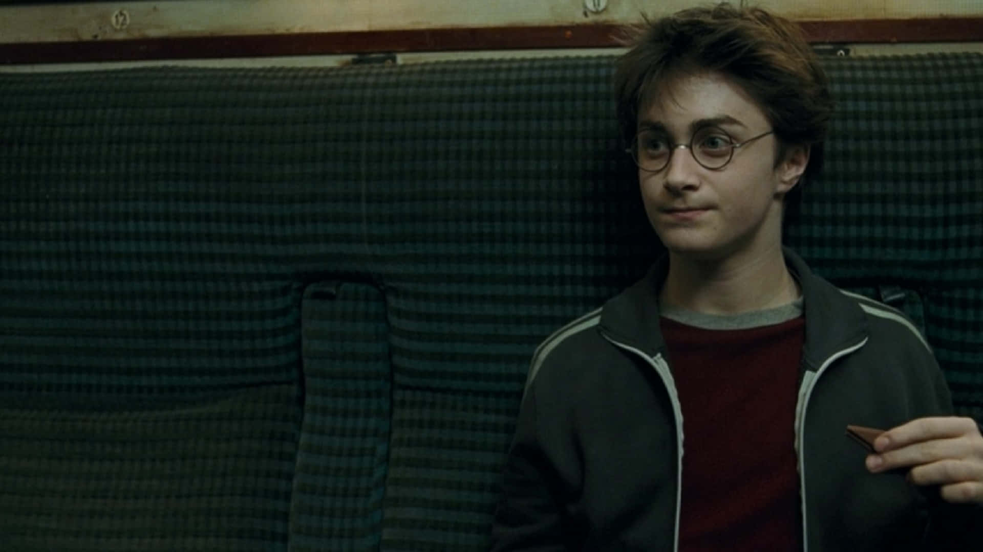 The Prisoner Of Azkaban 桌布 壁紙 — 年輕的哈利波特坐在格子火車座位上，拿著一隻巧克力蛙，表情若有所思。
