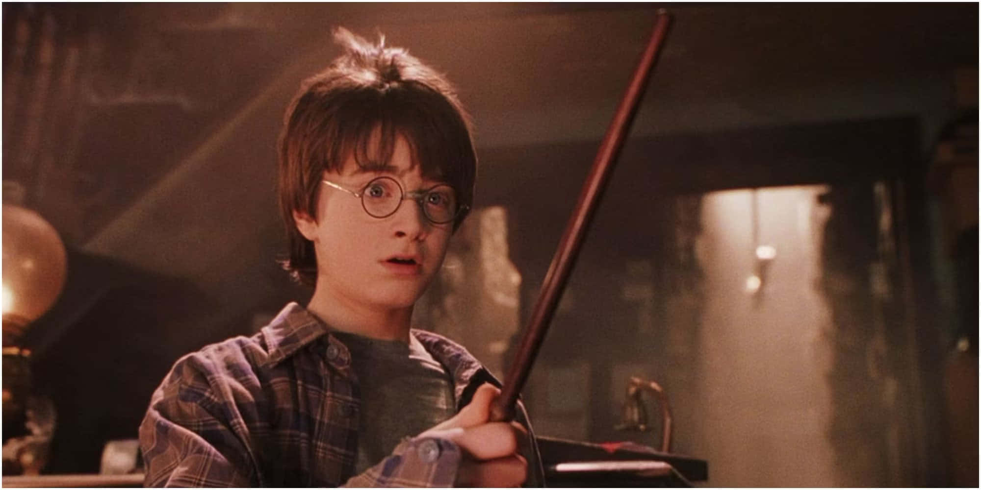 Harry Potter Profile 桌布 壁紙 — 年輕的哈利波特戴著圓框眼鏡，在一個光線昏暗、帶有溫暖燈光和發光燈的房間裡握著他的魔杖。