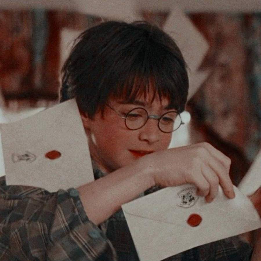 hp aesthetic 桌布 壁紙 — 年輕的哈利波特戴著圓框眼鏡，手持一封以紅色火漆封緘的霍格華茲入學信。