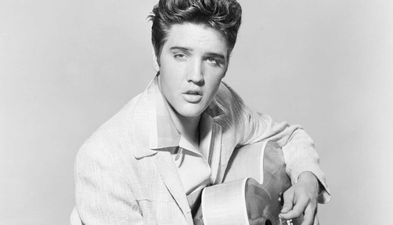 4K Elvis 桌布 壁紙 — 年輕的埃爾維斯·普雷斯利在簡樸的攝影棚背景下，專注地凝視著，手中拿著一把原聲吉他。