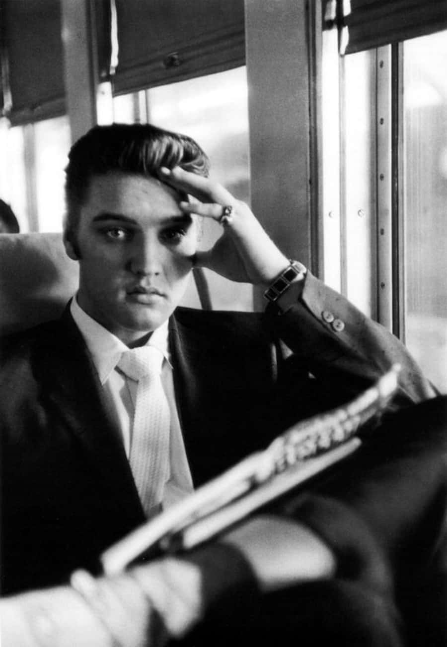 Elvis 桌布 壁紙 — 年輕的埃爾維斯·普雷斯利身穿西裝，在火車車廂內專注地凝視著，手持吉他，陽光透過窗戶照射進來。