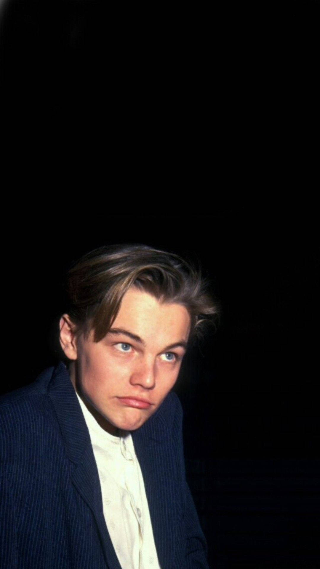 Dicaprio 桌布 壁紙 — 年輕的李奧納多·狄卡皮歐穿著細條紋西裝和白襯衫，在純黑背景下專注地凝視。