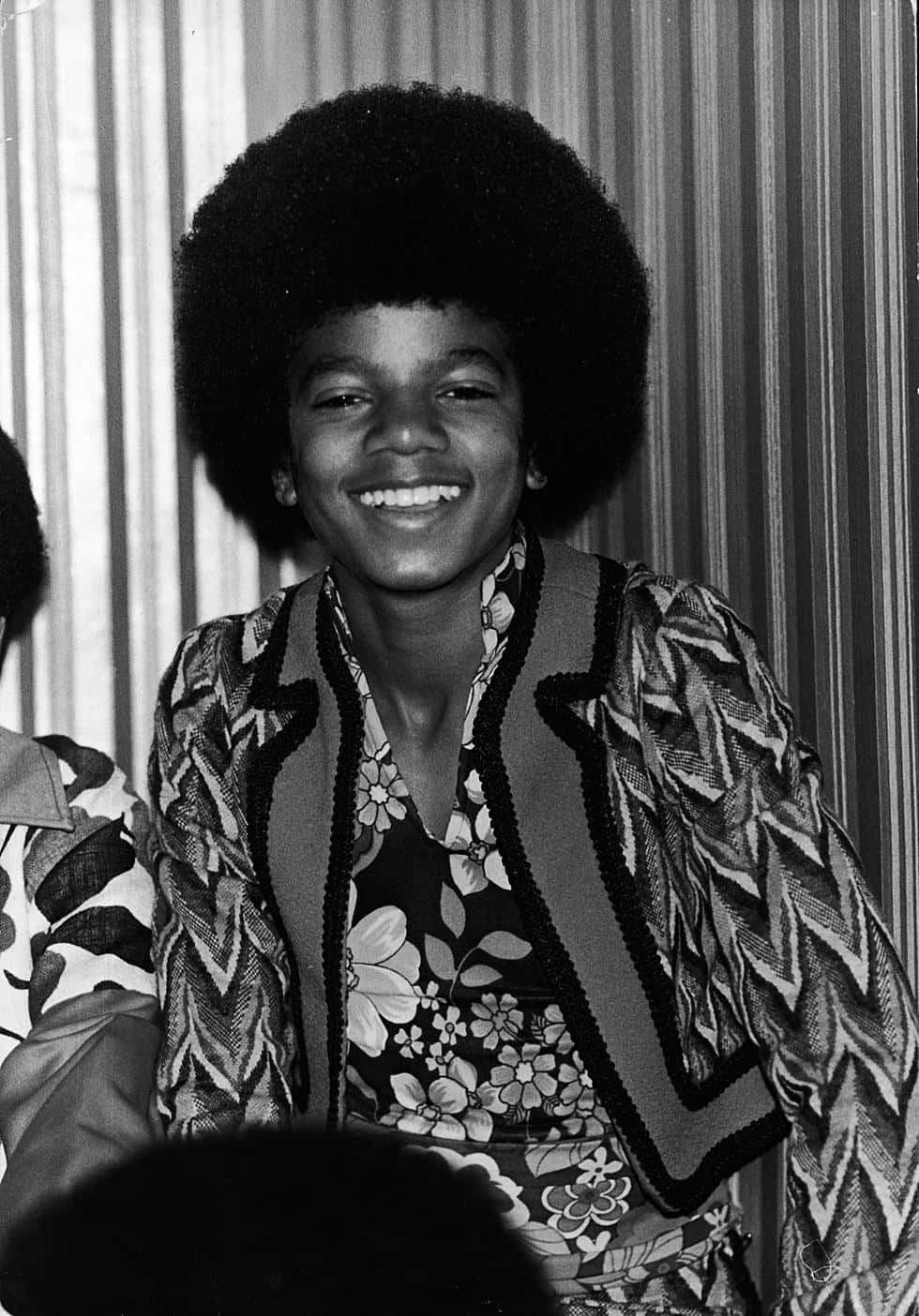 Young Michael Jackson 桌布 壁紙 — 年輕的麥可傑克森在條紋壁紙前穿著大膽的70年代花卉服裝，洋溢著喜悅。