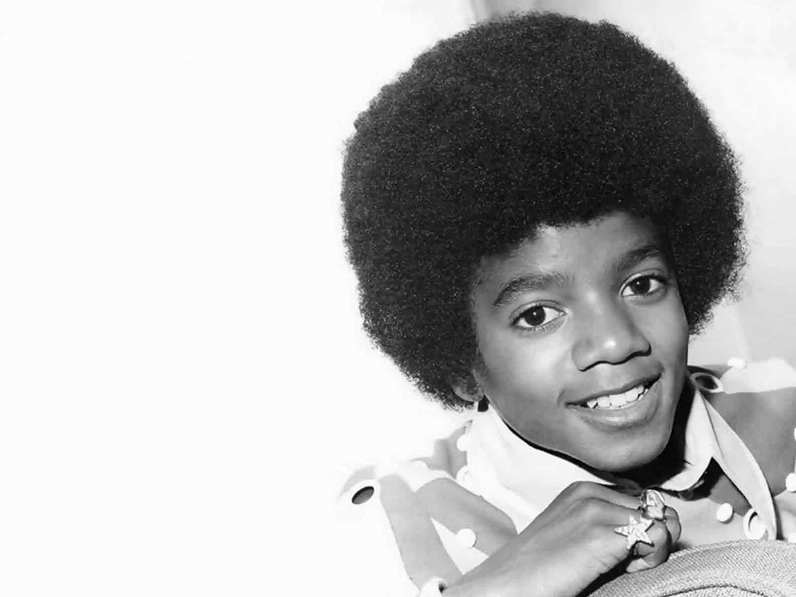Young Michael Jackson 桌布 壁紙 — 年輕的麥可傑克森在純白背景下，帶著蓬鬆的非洲式髮型和星形戒指，露出燦爛的笑容。