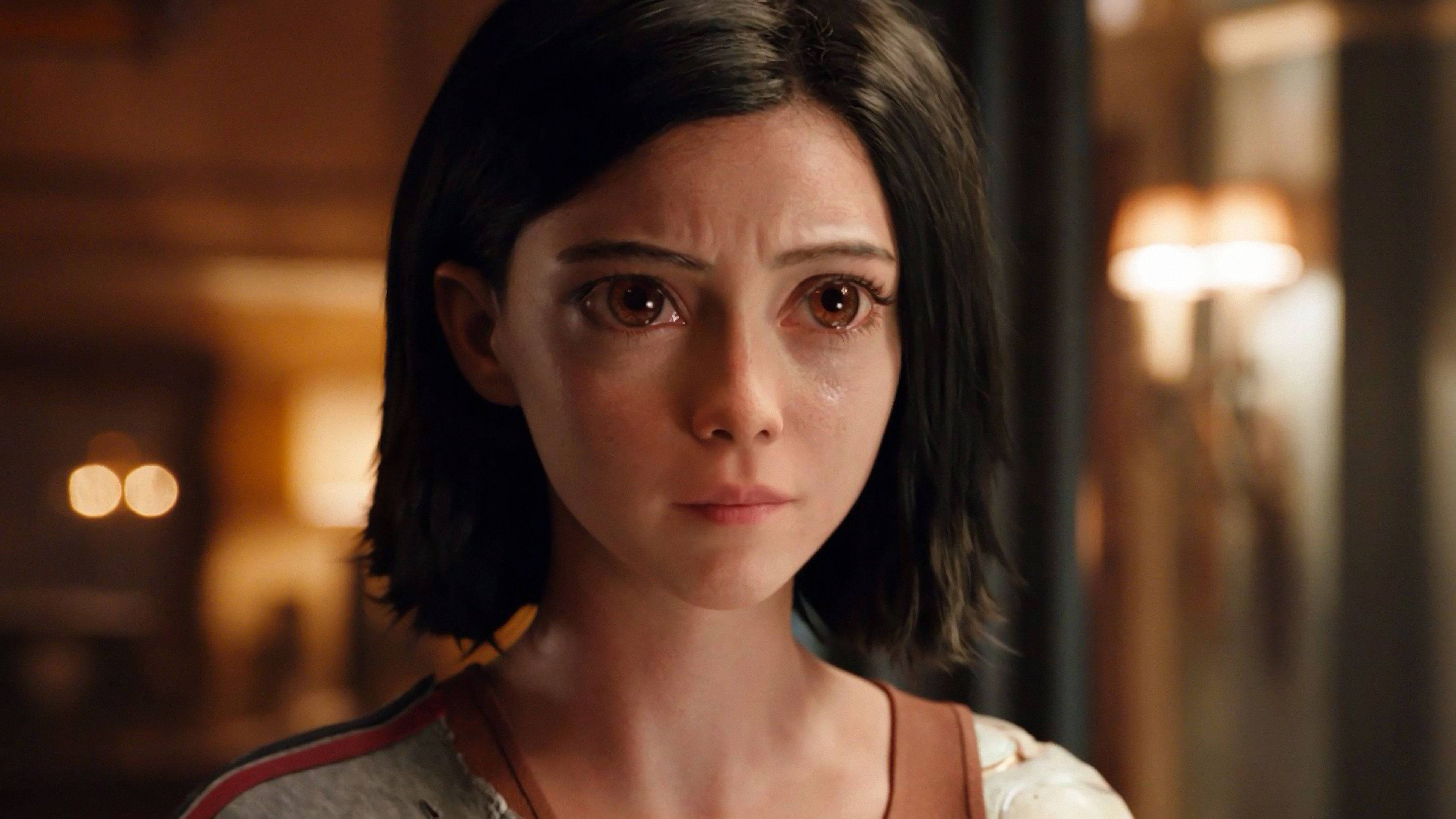 Alita 桌布 壁紙 — 年輕黑髮女子特寫，臉頰帶淚痕，在溫暖室內燈光下凝視。