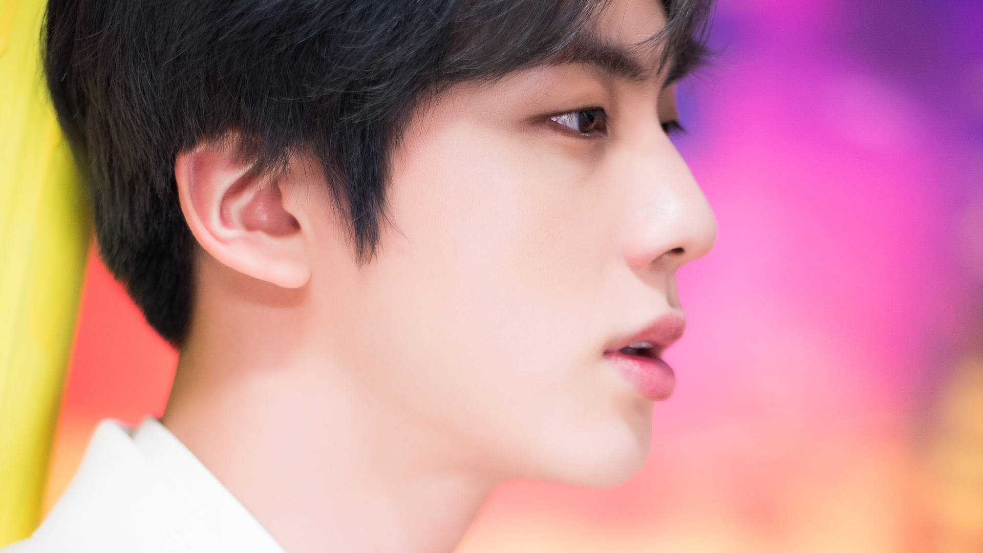 Jin 桌布 壁紙 — 年輕黑髮男子的特寫側面，背景是充滿活力的粉紅、黃色和橙色模糊色調。