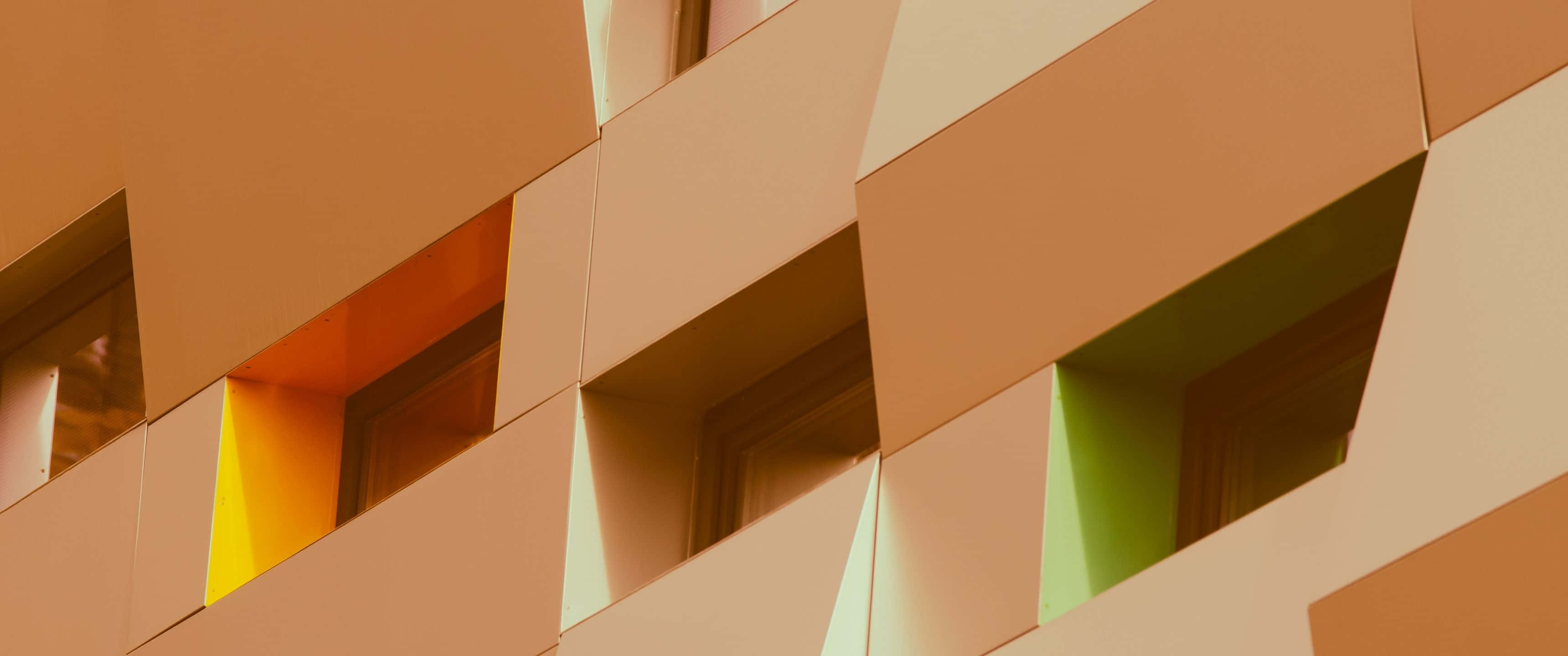 3440x1440 桌布 壁紙 — 幾何現代建築外牆，採用溫暖的橙米色面板和彩色嵌入式窗戶。