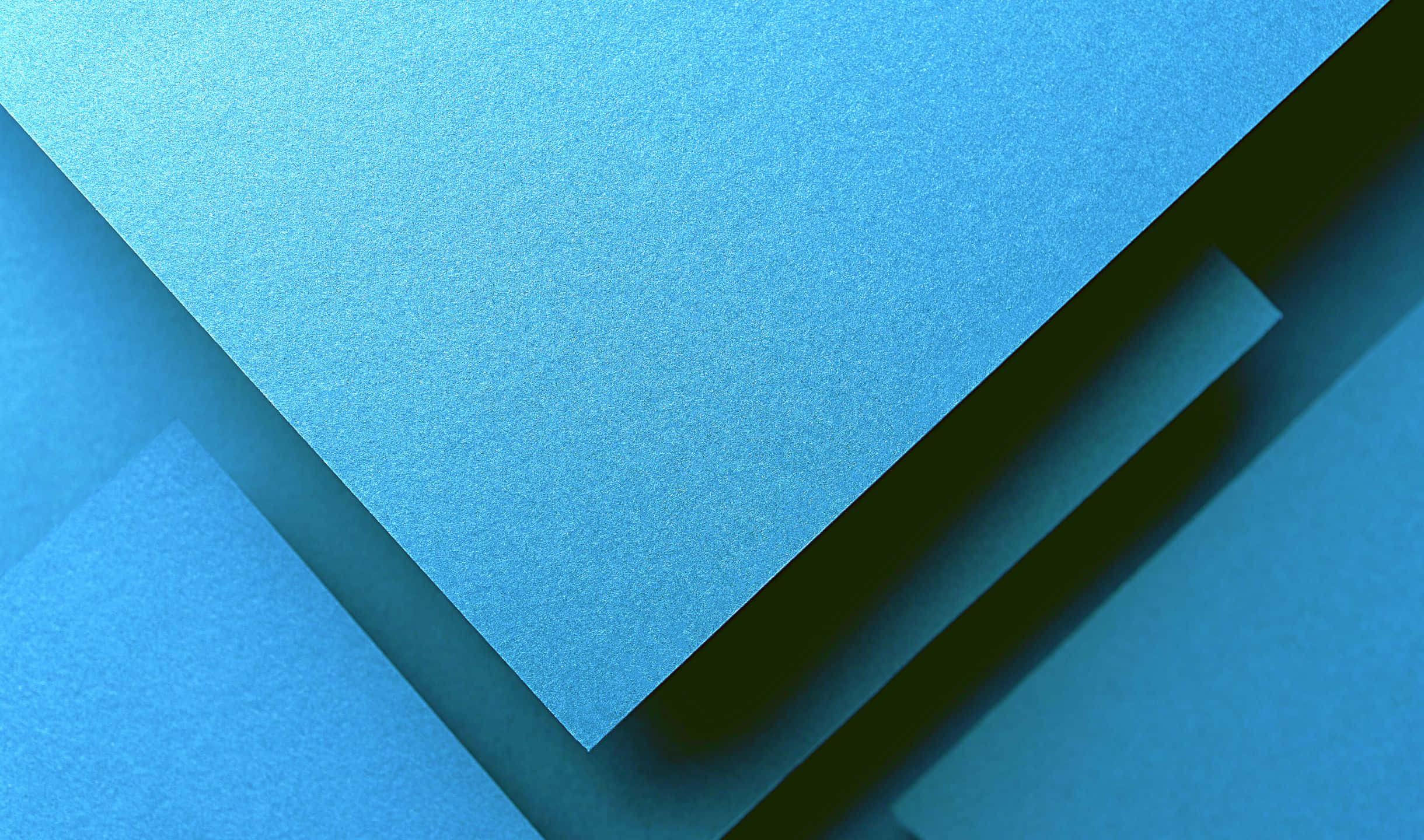2440x1440 Material 桌布 壁紙 — 幾何藍色紙飛機在柔和陰影中重疊，營造出極簡抽象構圖。