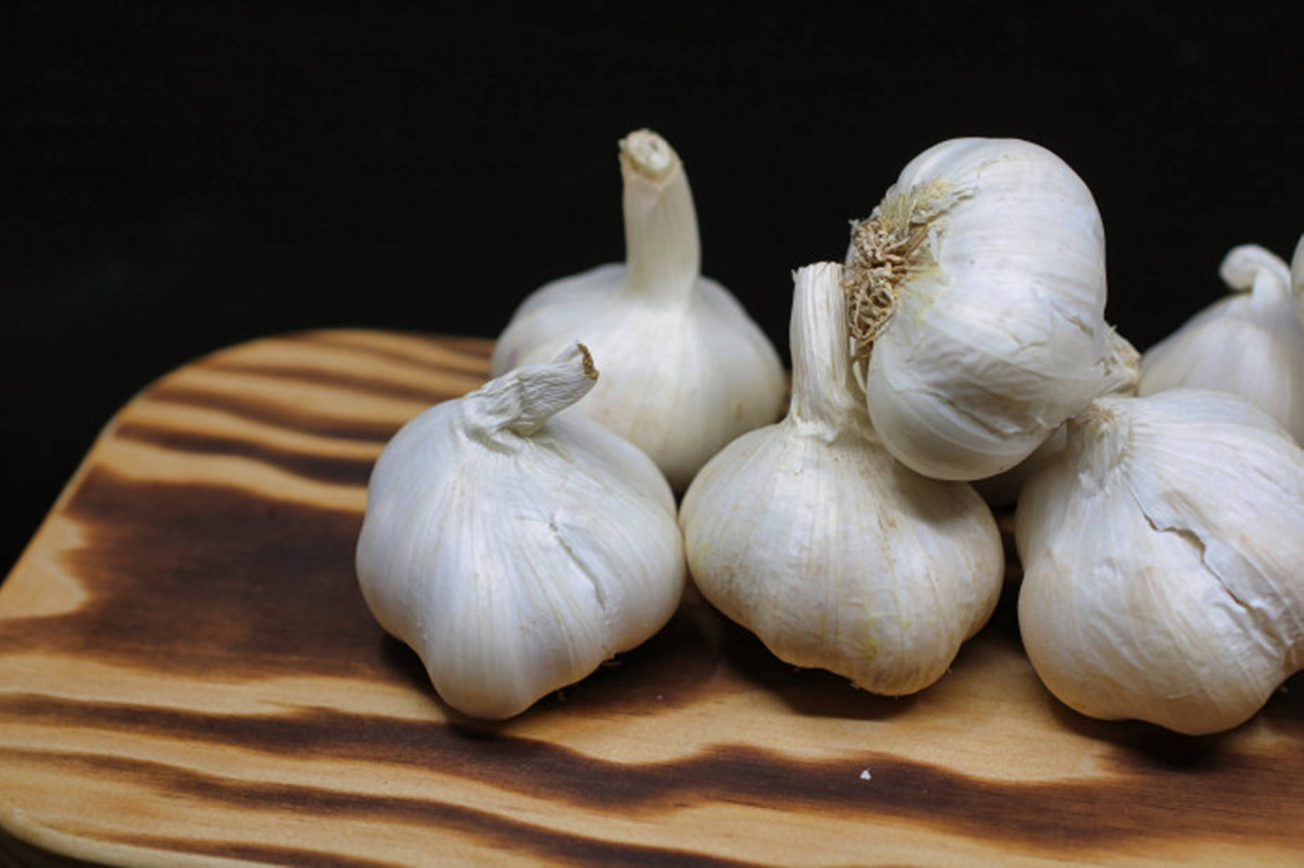 Garlic 桌布 壁紙 — 幾個新鮮的白蒜頭放在有條紋的木砧板上，背景為深色。