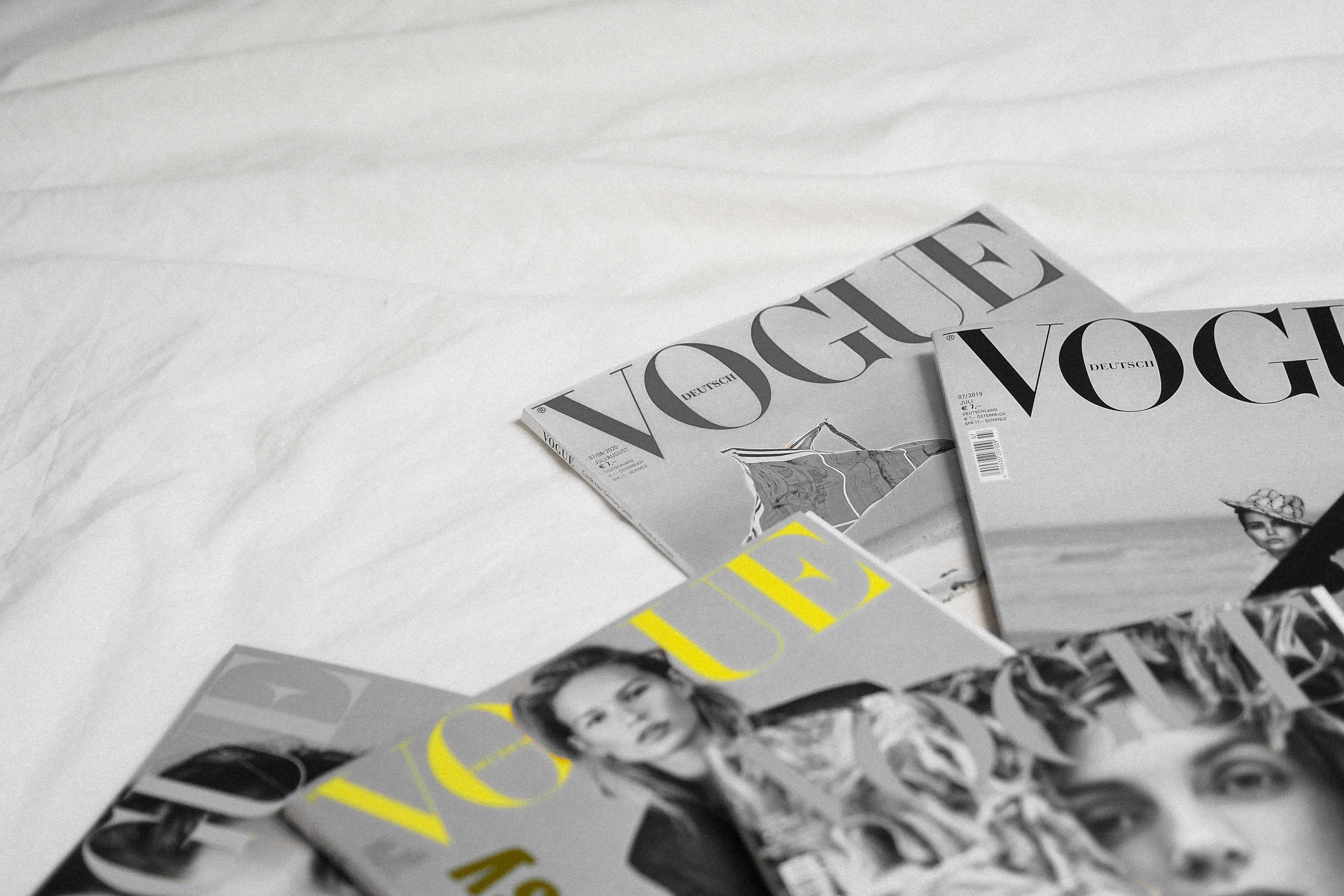 雜誌 桌布 壁紙 — 幾本Vogue雜誌，帶有粗體字體和時尚圖像，隨意地放在皺巴巴的白色床單上。