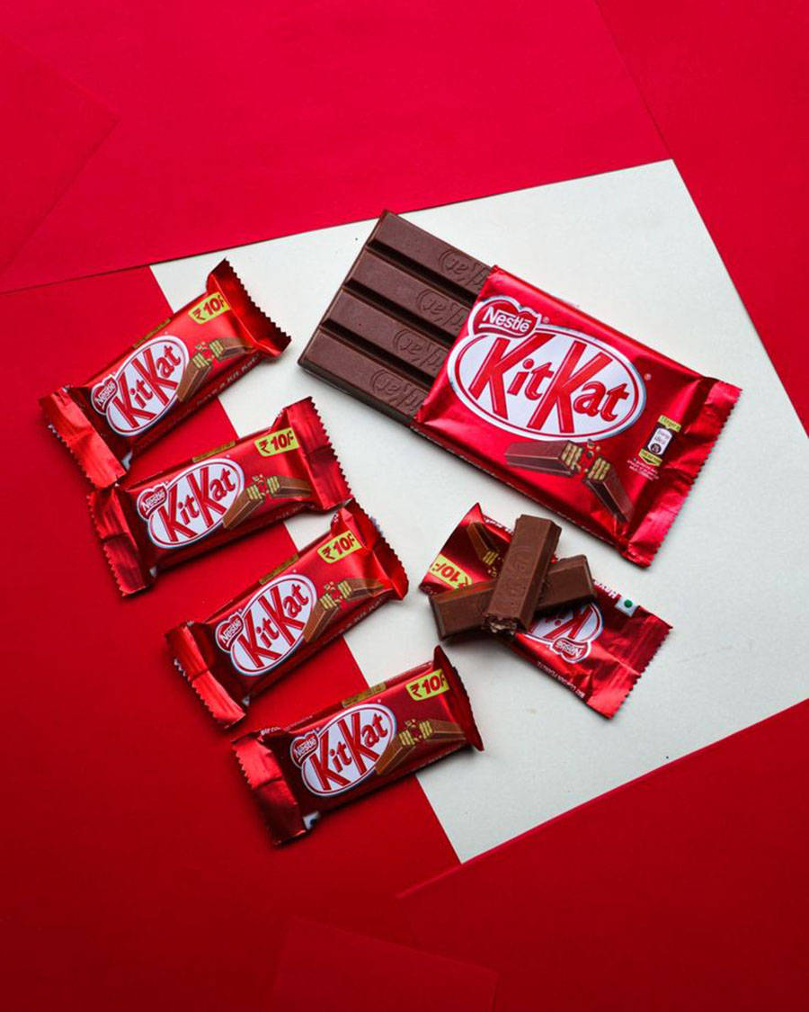 Chocolate 桌布 壁紙 — 幾條KitKat巧克力棒和碎塊排列在鮮明的紅白幾何背景上。