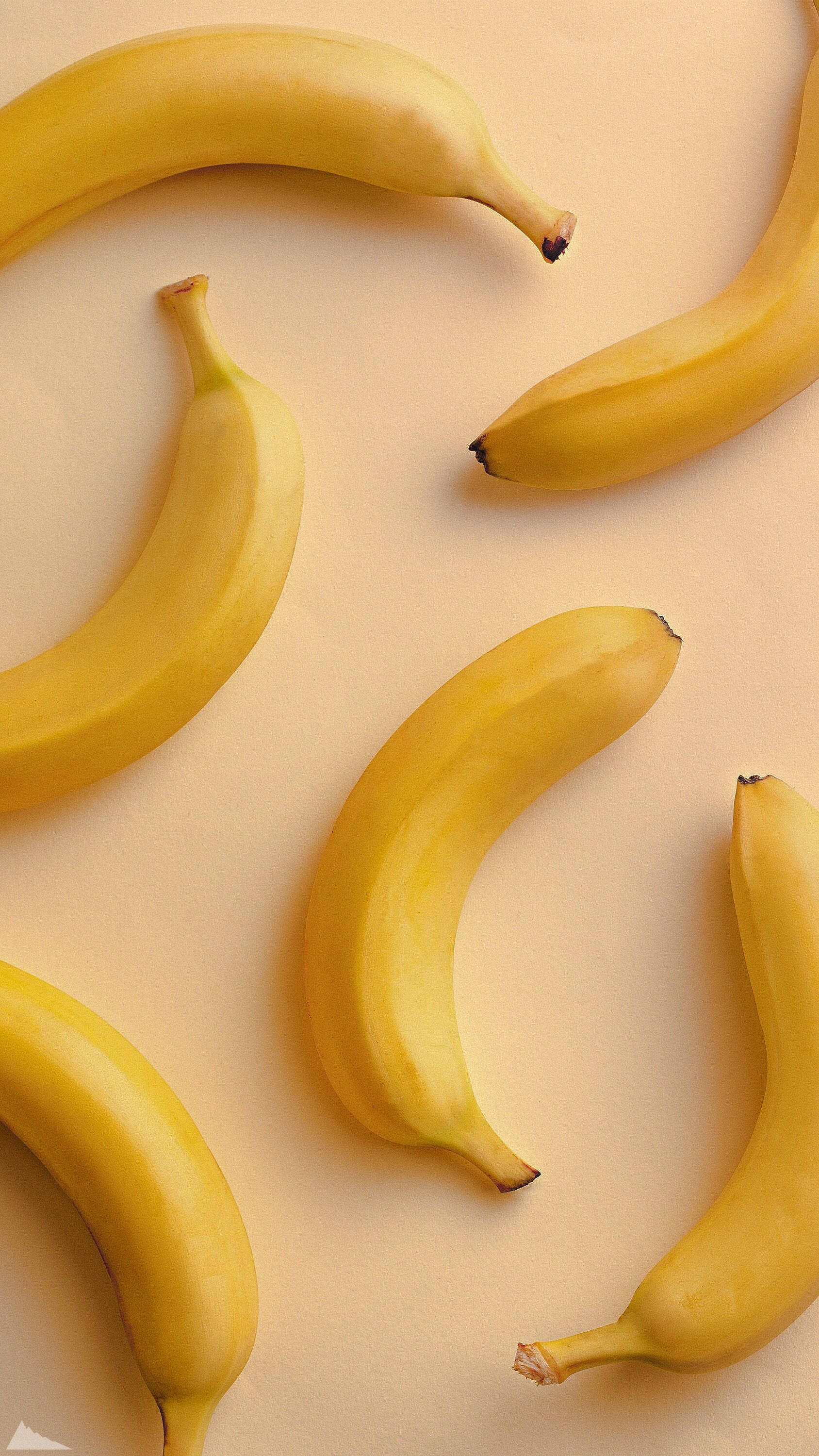 Plantain 桌布 壁紙 — 幾條成熟的黃色香蕉以分散的圖案排列在柔軟的米色背景上。