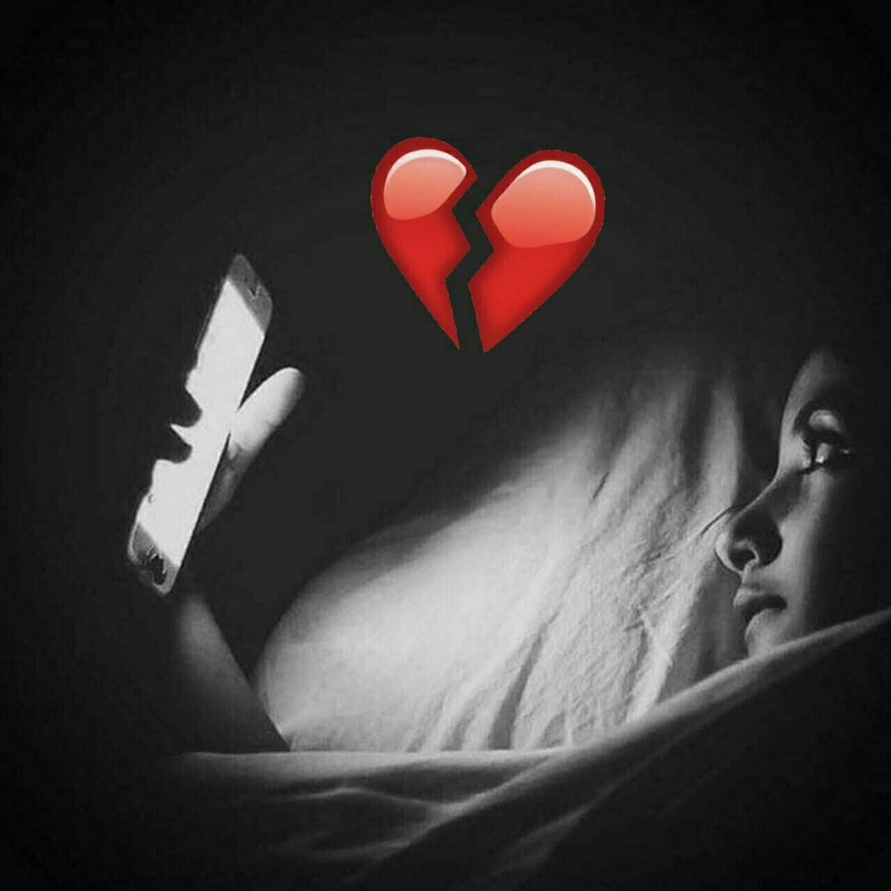 Broken Heart Sad 桌布 壁紙 — 床上的人凝視著手機，一個發光的紅色心碎表情符號懸浮在上方，在昏暗燈光中傳達心碎之情。