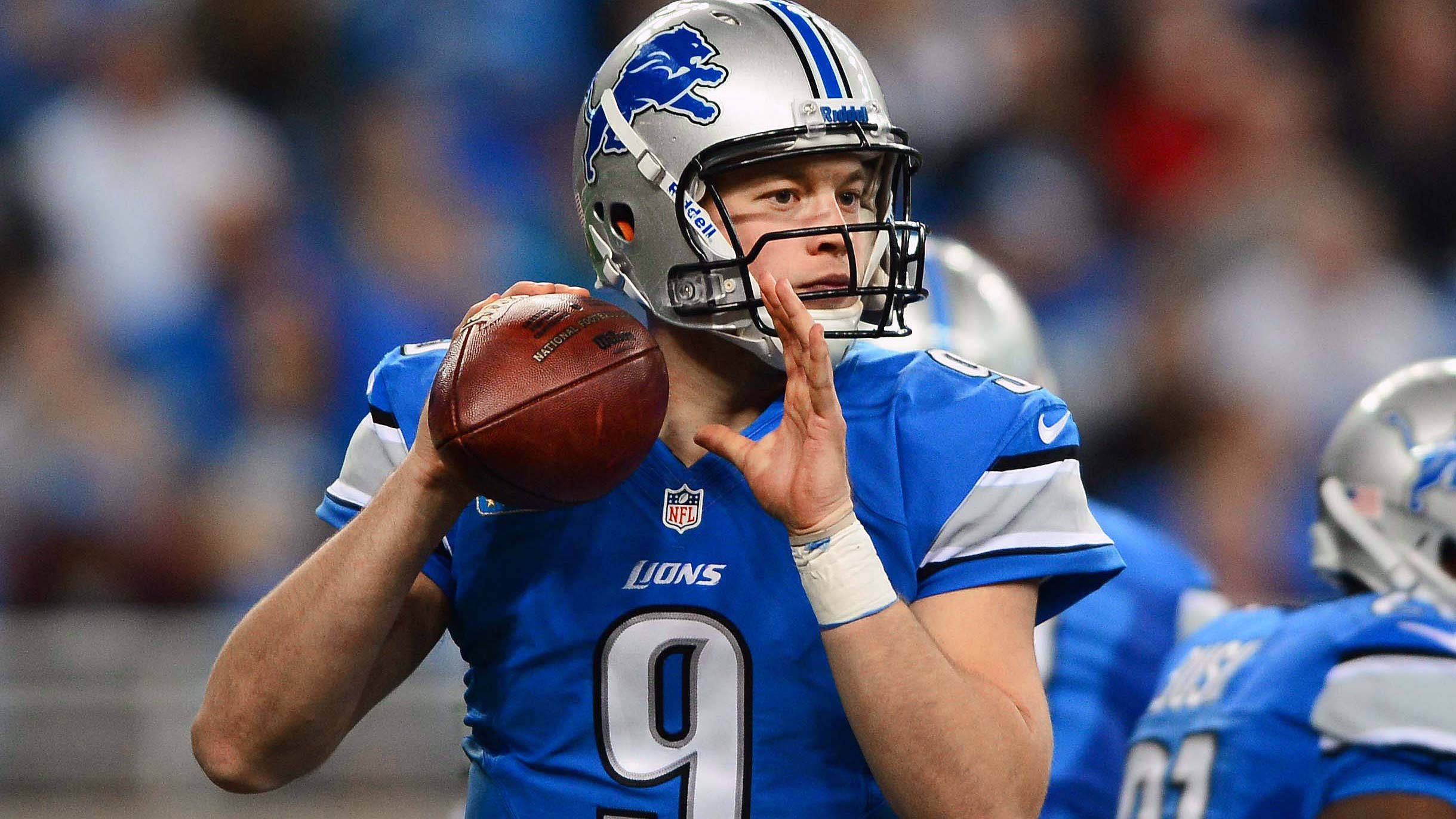 Matthew Stafford 桌布 壁紙 — 底特律雄獅隊的四分衛身穿藍色球衣，在體育場燈光下準備在比賽中擲出橄欖球。