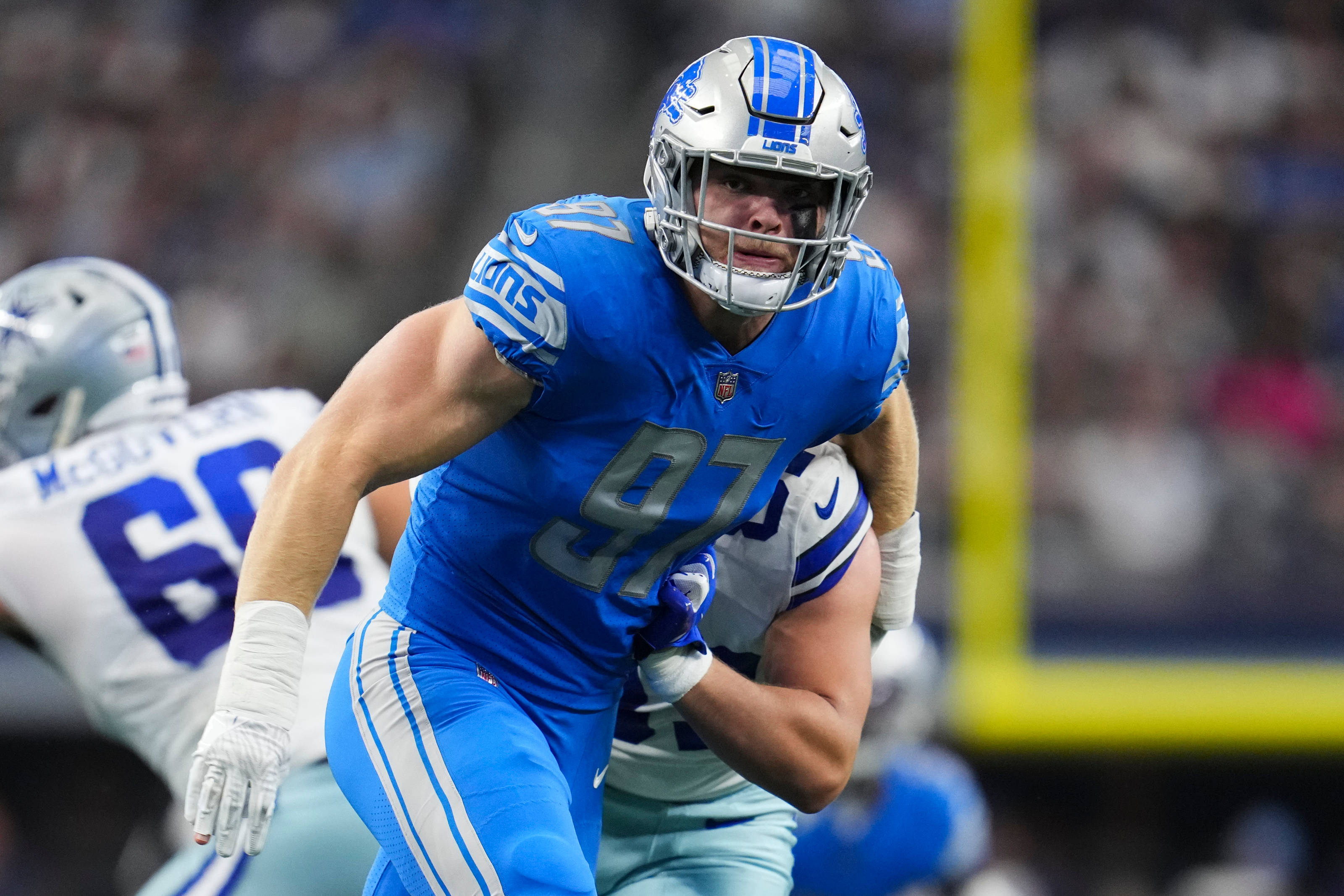 Detroit Lions 桌布 壁紙 — 底特律雄獅隊的藍色制服美式足球員在夜間比賽中，於球場燈光下擒抱對手。