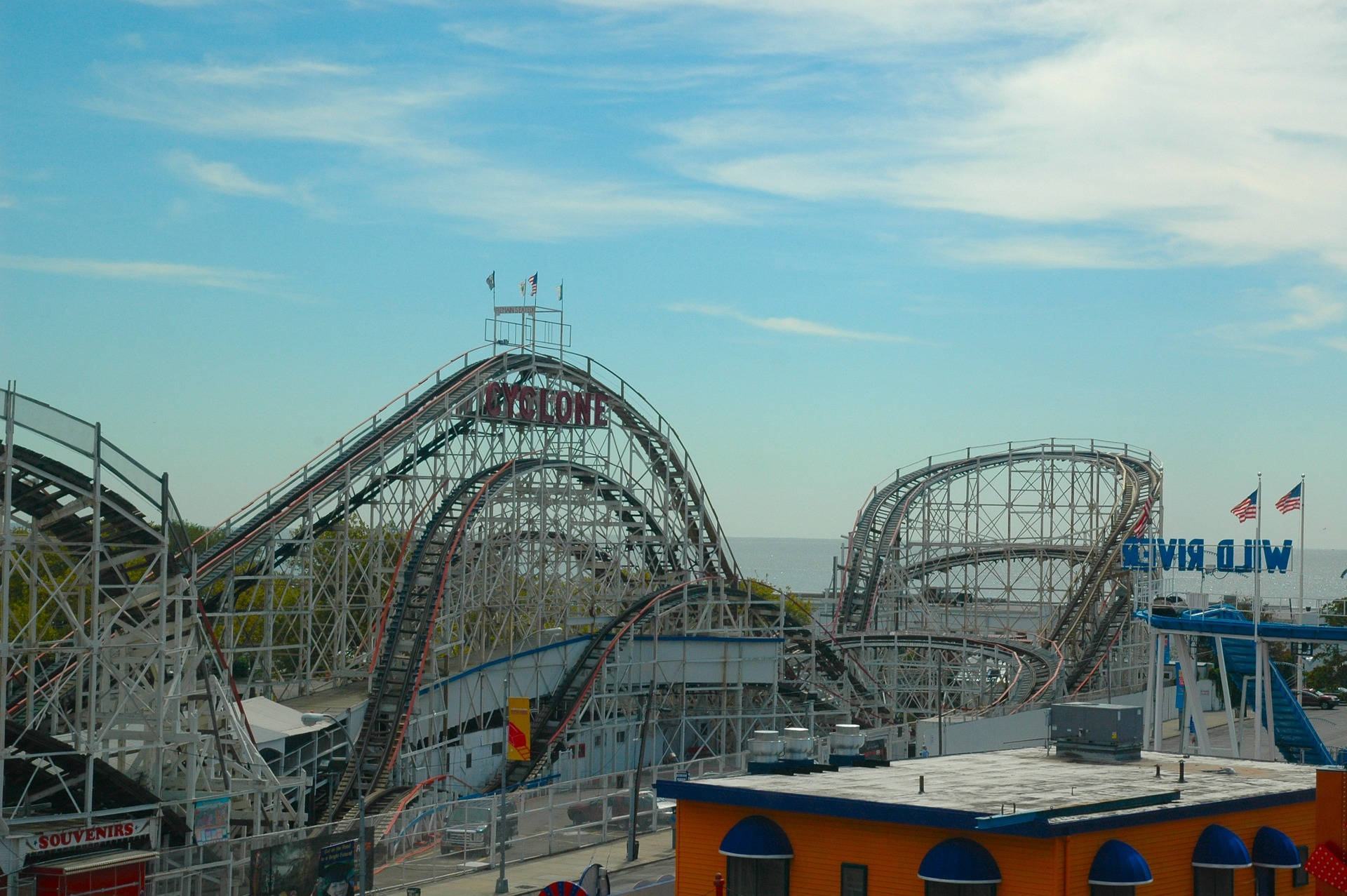 Roller Coaster 桌布 壁紙 — 康尼島晴朗的一天，標誌性的旋風雲霄飛車聳立在色彩繽紛的遊樂園建築和遠處的海洋之上。