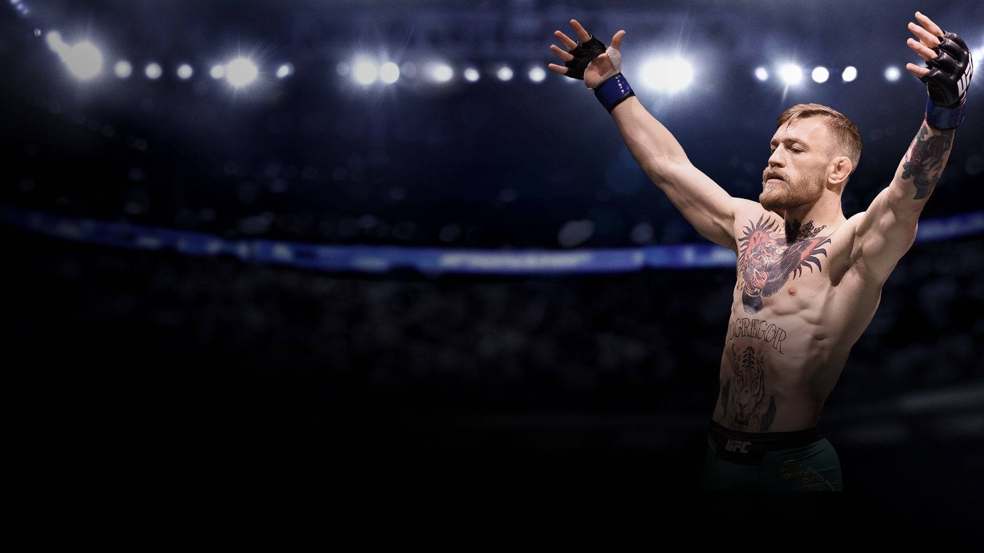 UFC 桌布 壁紙 — 康納·麥格雷戈在體育場燈光下，於明亮照明的UFC八角籠中勝利地舉起雙臂。