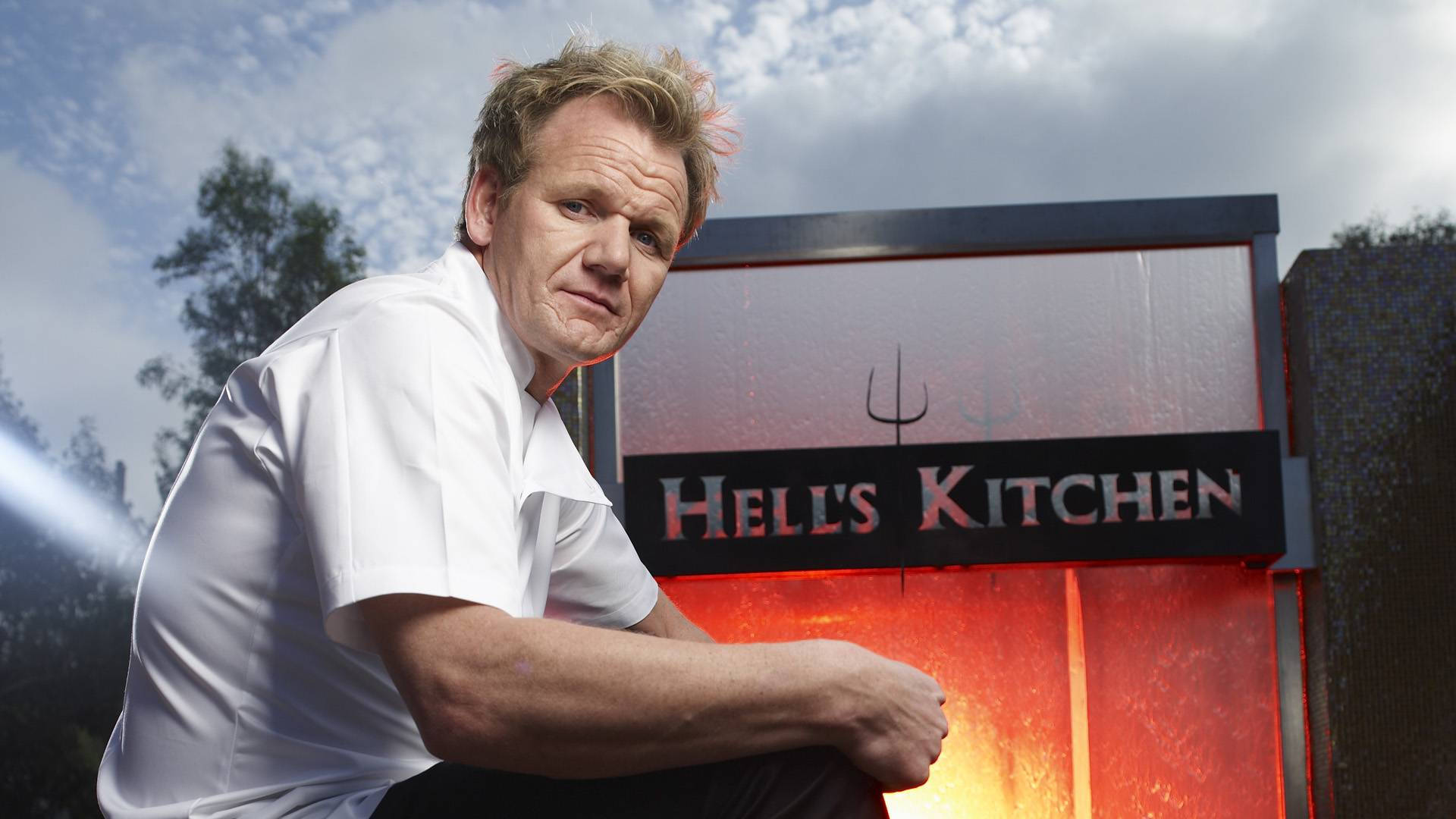 Gordon Ramsay 桌布 壁紙 — 廚師戈登·拉姆齊在陰天之下，強烈地坐在發光的Hell's Kitchen標誌前。