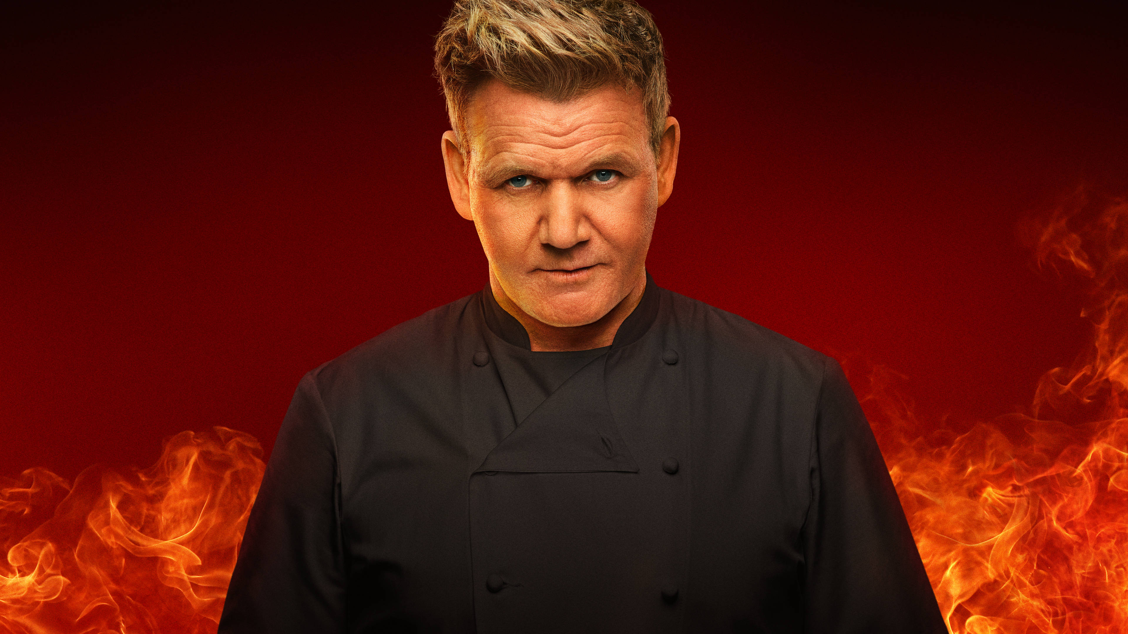 Gordon Ramsay 桌布 壁紙 — 廚師戈登·拉姆齊身穿黑色廚師外套，嚴肅地站在火紅背景前，兩側有火焰旋轉。