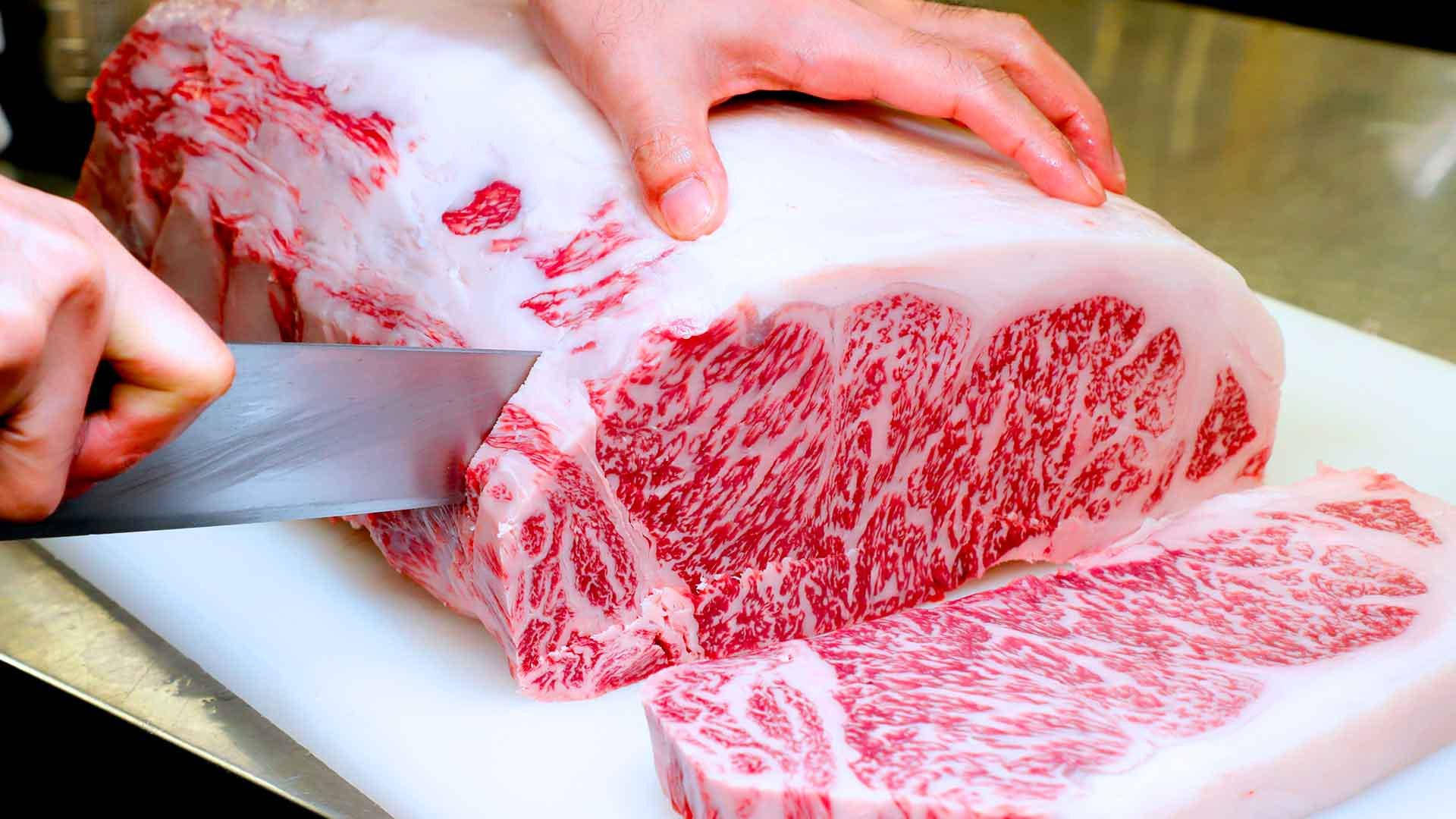 meat 桌布 壁紙 — 廚師正在白色砧板上切一大塊大理石紋和牛烤肉，露出複雜的紅白脂肪紋理。