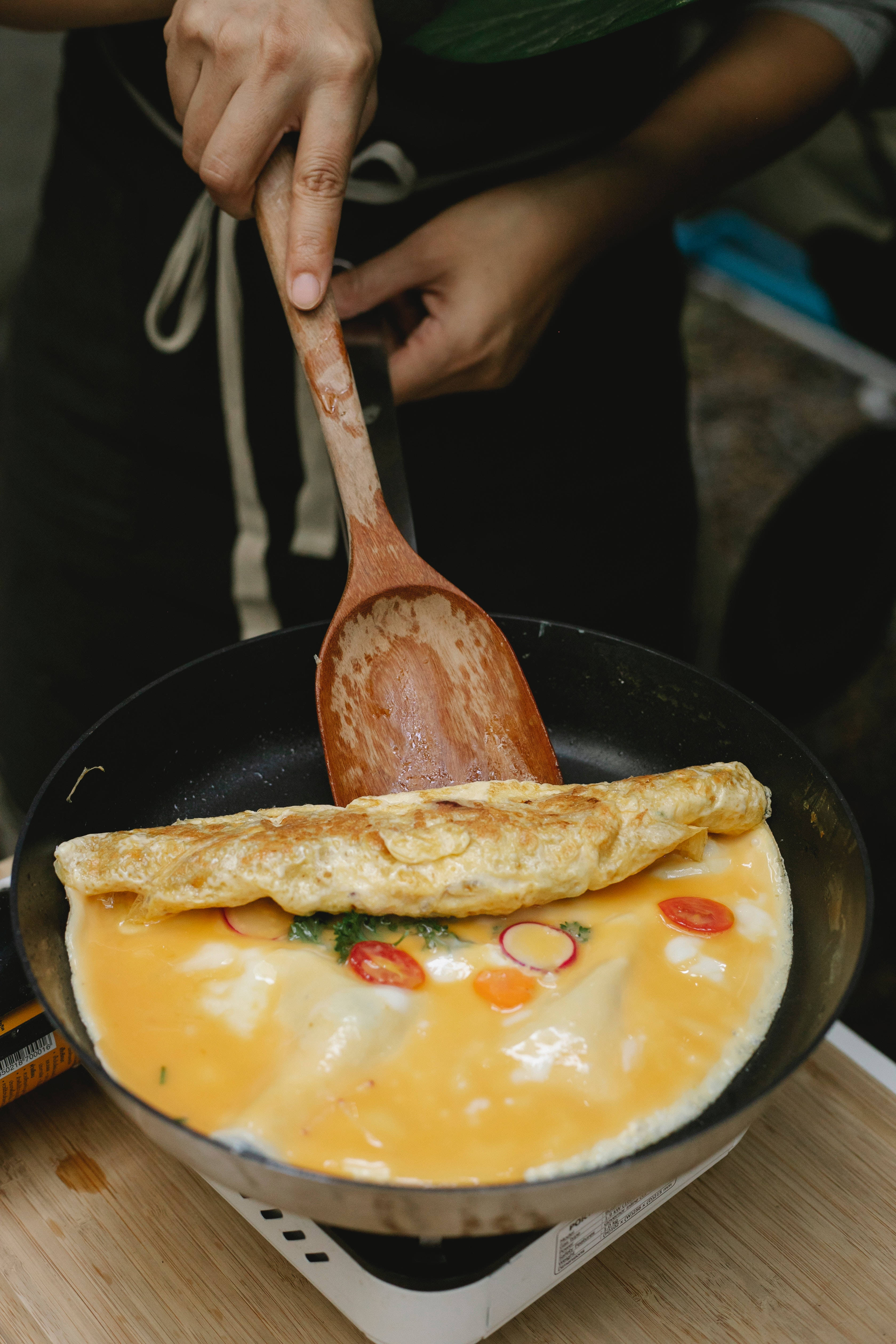 Egg 桌布 壁紙 — 廚師用木匙在黑色平底鍋中折疊金黃色歐姆蛋，露出融化起司和色彩繽紛的蔬菜。