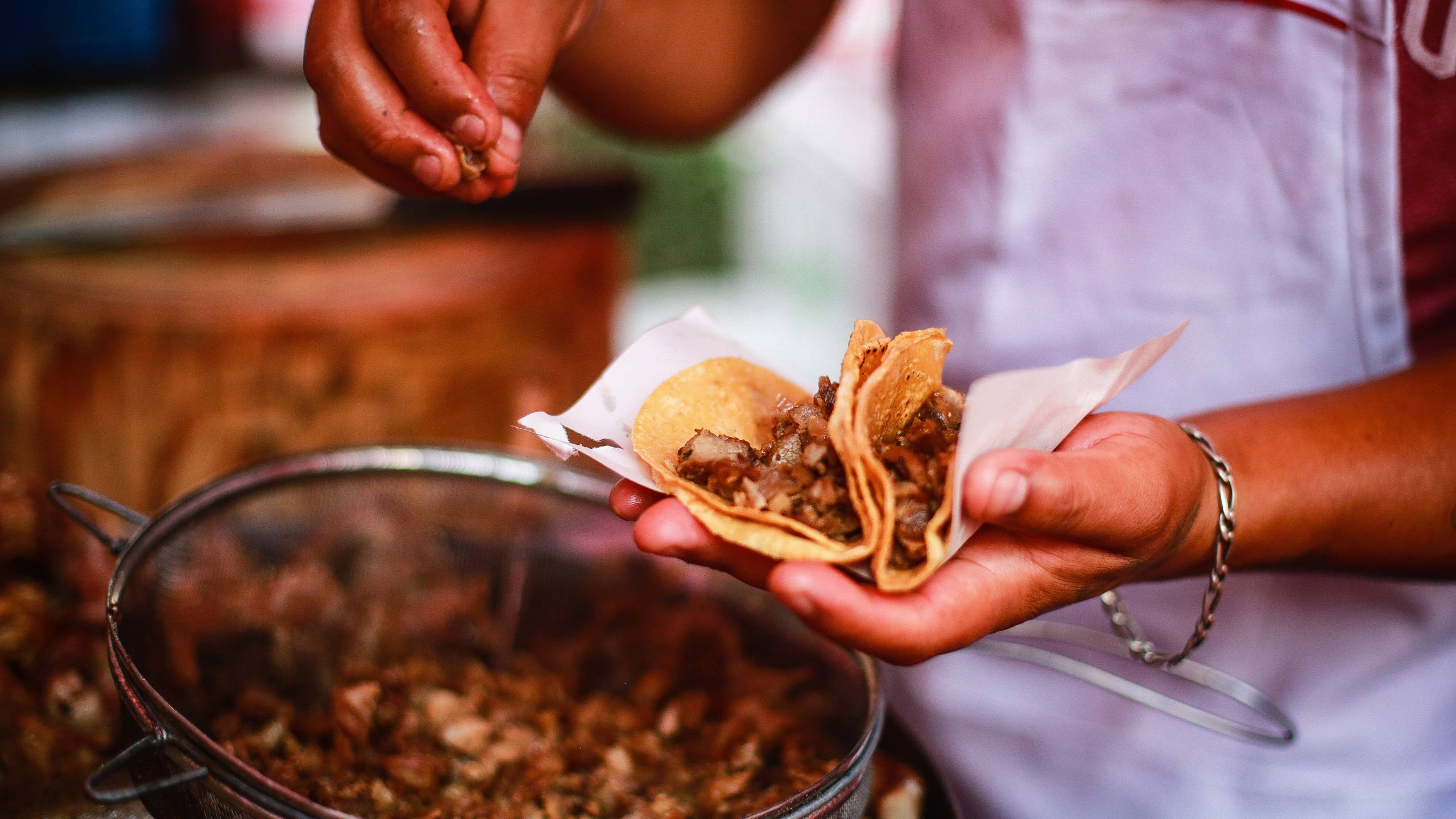 Mexican Food 桌布 壁紙 — 廚師的雙手在冒著蒸汽的肉鍋上，精緻地為兩個軟玉米餅添加新鮮配料。