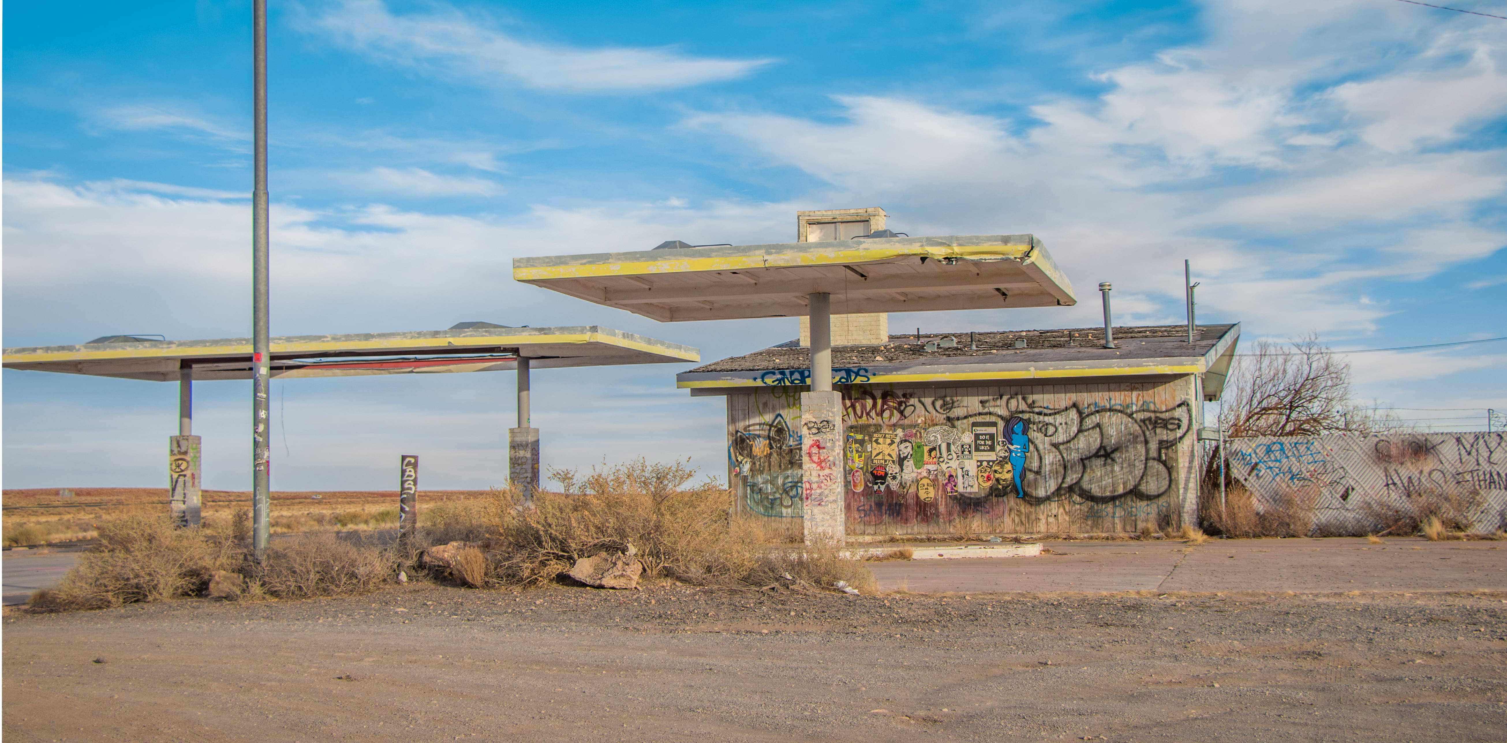 Gas Station 桌布 壁紙 — 廢棄加油站，牆上佈滿塗鴉，生鏽的油泵，明亮的藍天上有散落的雲朵。